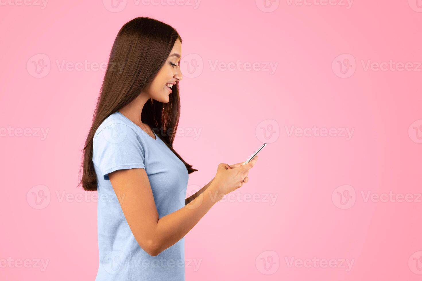 People, Technology And Communication Concept. Side view portrait of beautiful lady texting on her cell phone, isolated over yellow studio background, copy space. Smiling woman chatting in social media photo