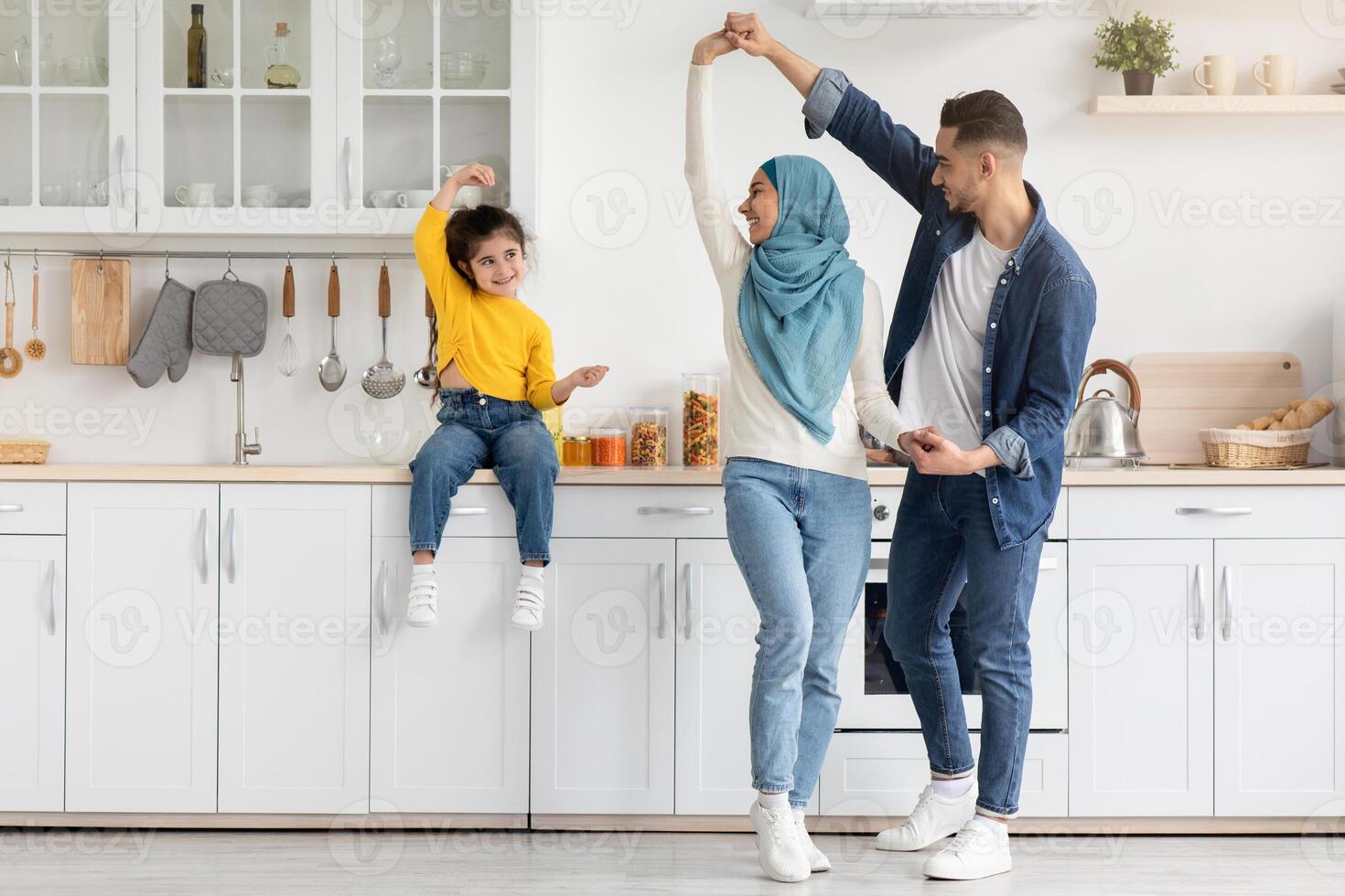 Happy Islamic Family With Little Daughter Having Fun Together In Kitchen, Cheerful Middle Eastern Parents And Their Cute Female Child Dancing And Laughing, Enjoying Spending Time At Home photo