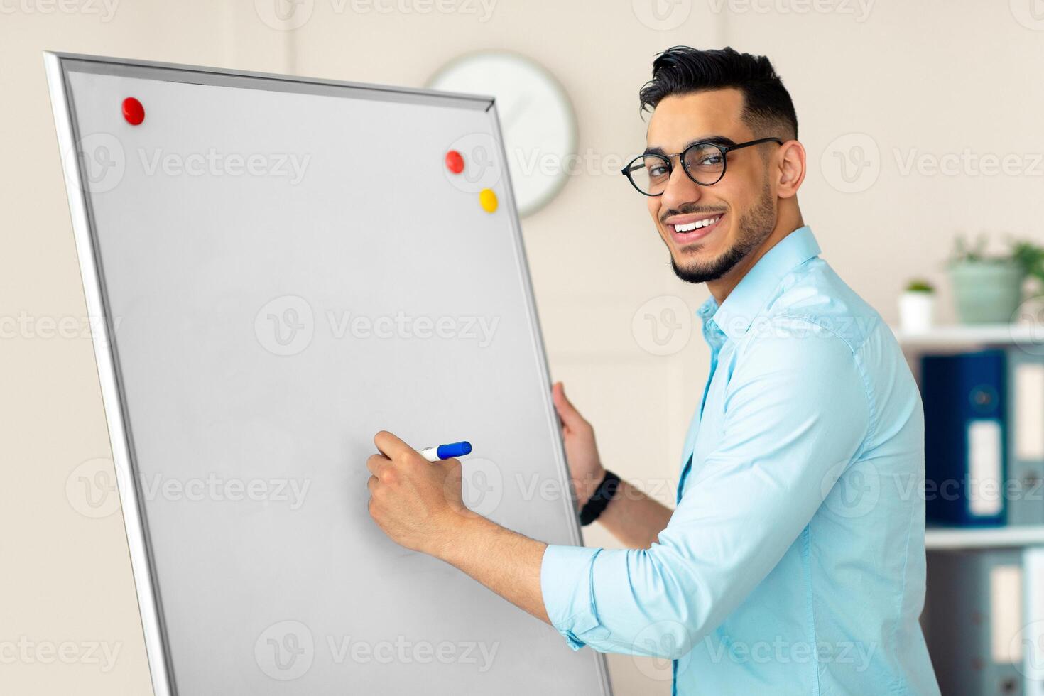 Young Arab guy teacher giving online class, explaining new material, writing English rules on blackboard at home office. Remote tutoring and distance education during coronavirus concept photo