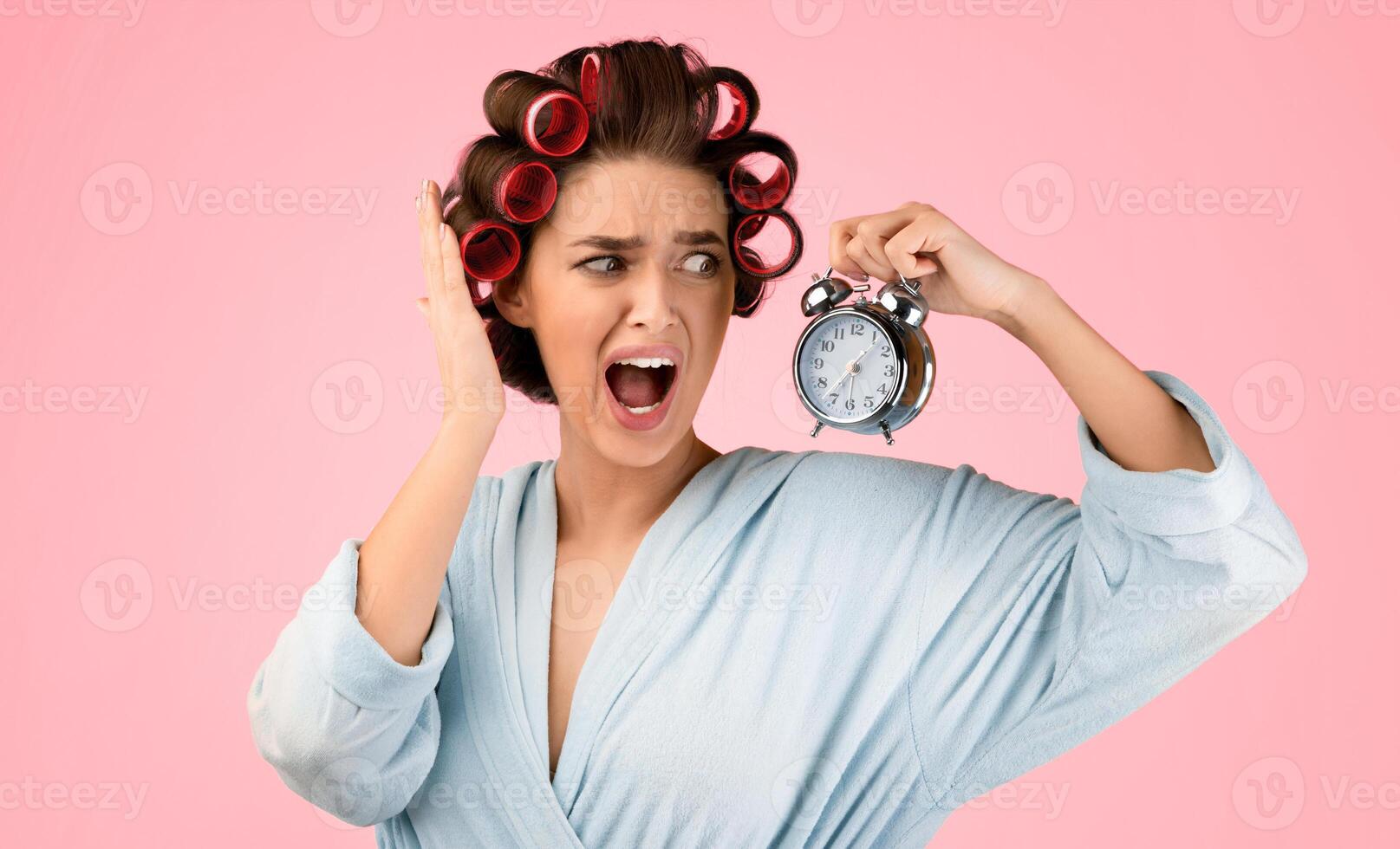 I'm Late. Emotional Lady With Hair Curlers Shouting Holding Clock Checking Time In A Hurry, Having Deadline Posing Standing Over Yellow Background. Studio Shot. Not In Time Concept photo