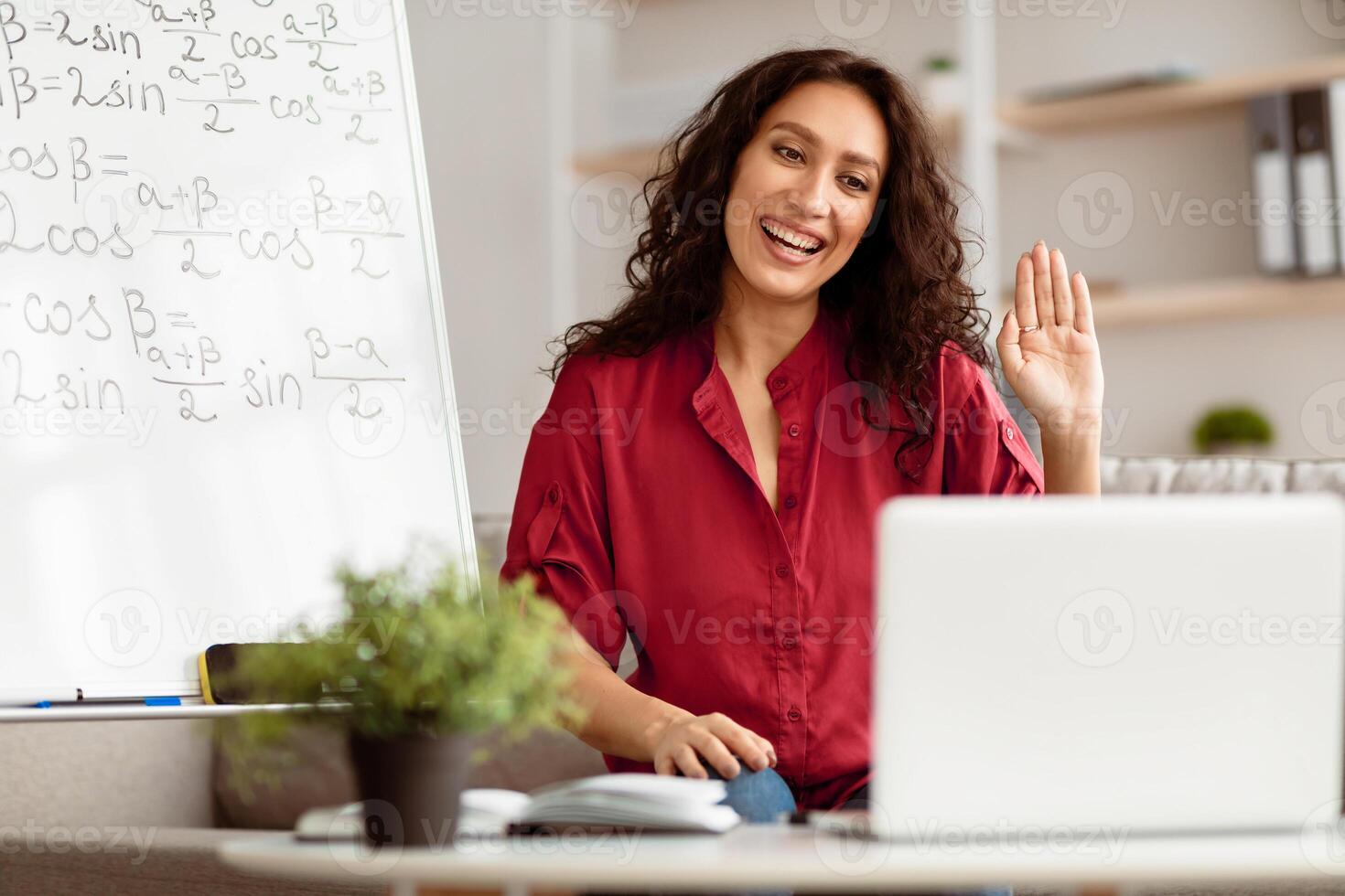 Distance Education. Portrait of positive lady having virtual meeting, sitting at desk, having call with students on laptop, waving hand to webcam. Woman teaching math science online at home photo