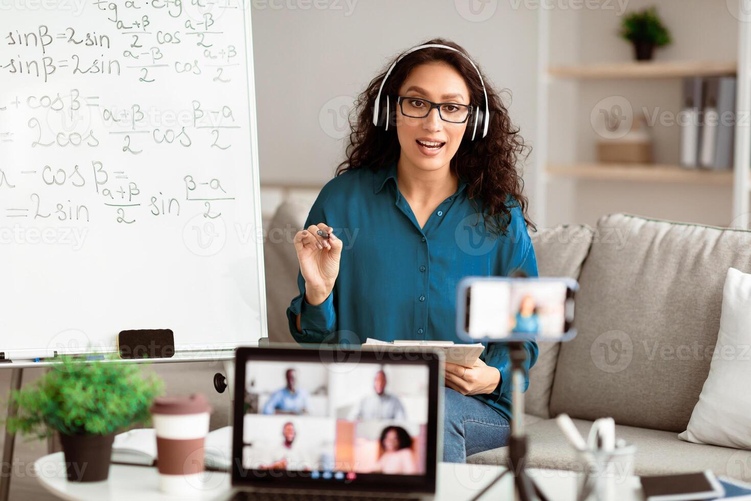 Online Education. Lady professor in eyeglasses and headphones teaching remotely working from home, teacher telling algebra information to group of diverse students on computer monitor photo