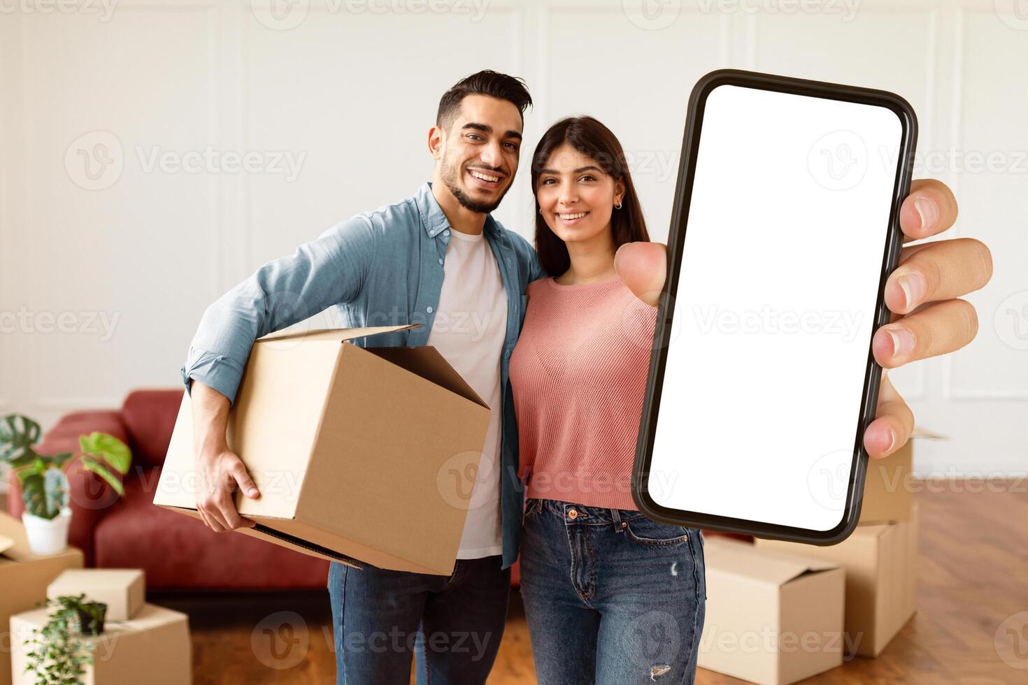 House Ownership. Young Couple Showing Keys And Holding Cardboard Box, Cheerful Guy And Lady Hugging After Moving In New Apartment Standing In Living Room. Insurance, Real Estate, Mortgage Concept photo