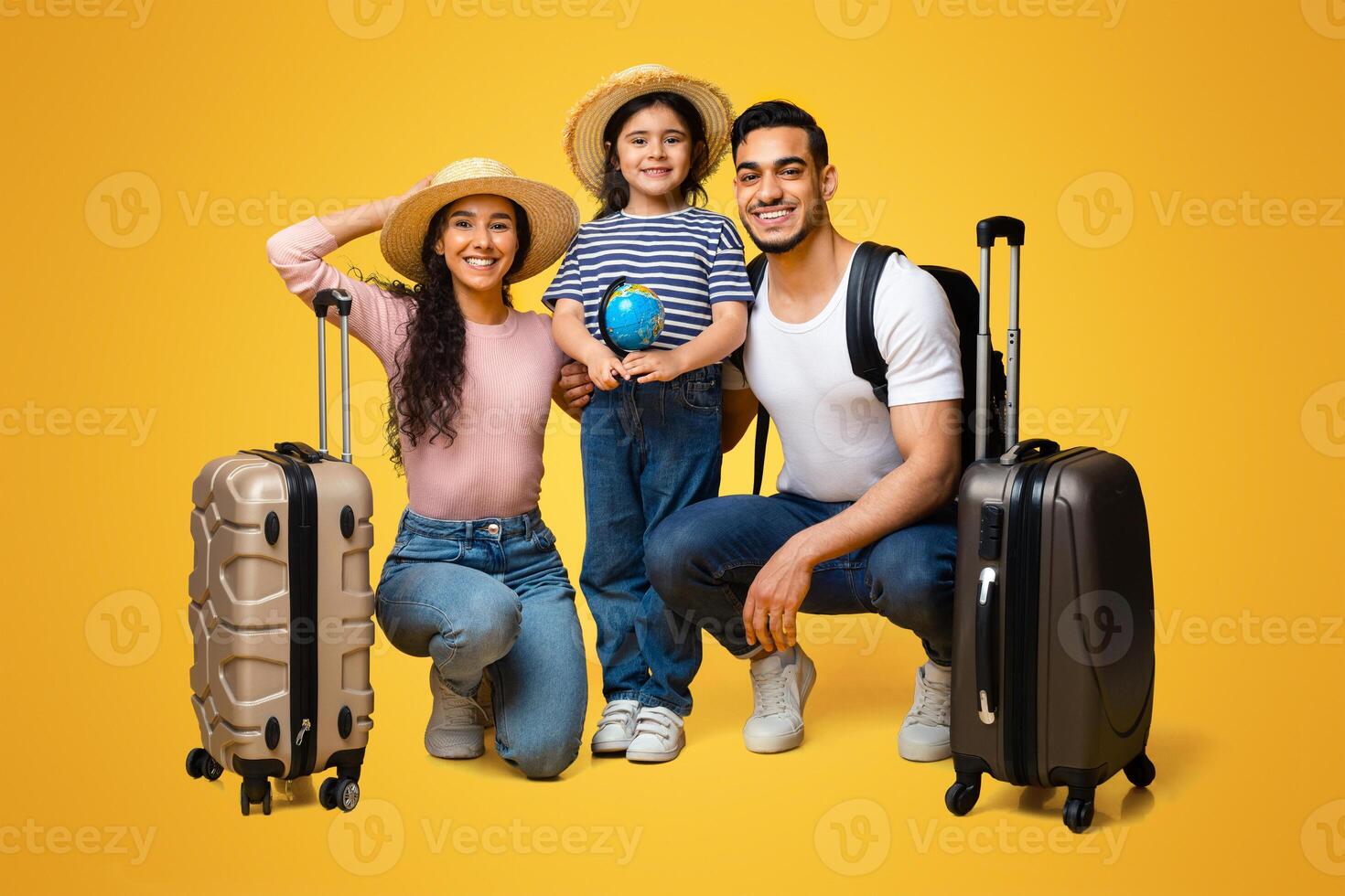 Ready For Vacation. Happy Arab Family Of Three With Suitcases Posing Together Over Yellow Background, Cute Little Middle Eastern Girl Holding Small Globe, Enjoying Travelling With Parents, Free Space photo