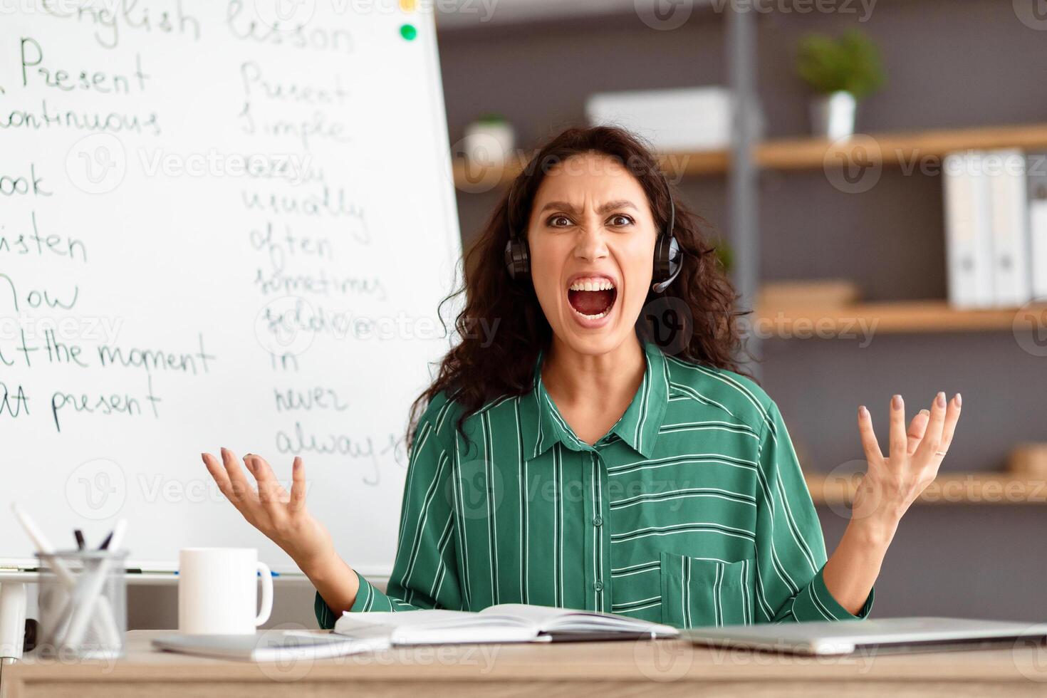 Professional Job Burnout. Portrait of exhausted angry lady tutor in headphones screaming out loud, irritated lady gesturing and looking at camera teaching English language online, sitting at desk photo