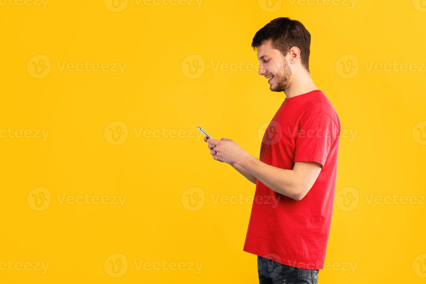 People, Technology And Communication Concept. Side view portrait of handsome man texting on his cell phone, isolated over blue studio background, copy space. Smiling guy chatting in social media photo