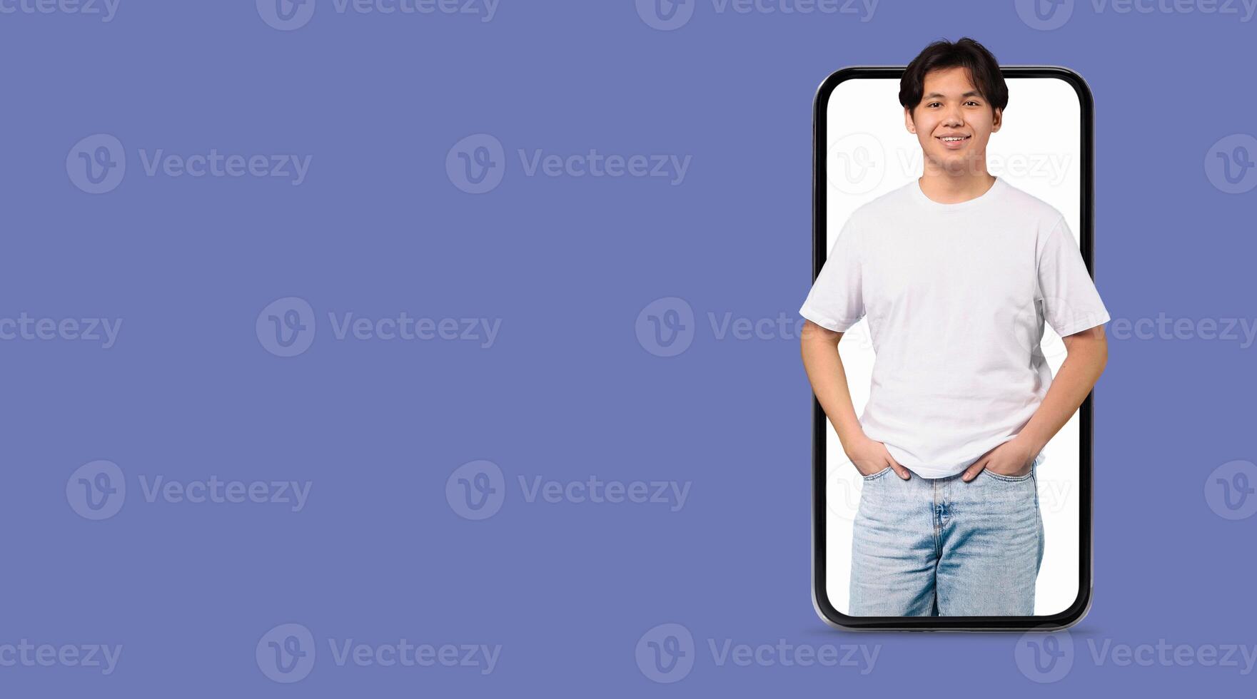 A young man stands confidently with his hands in pockets, positioned within a smartphone. He is ready to connect online using a social media application on the large screen. photo