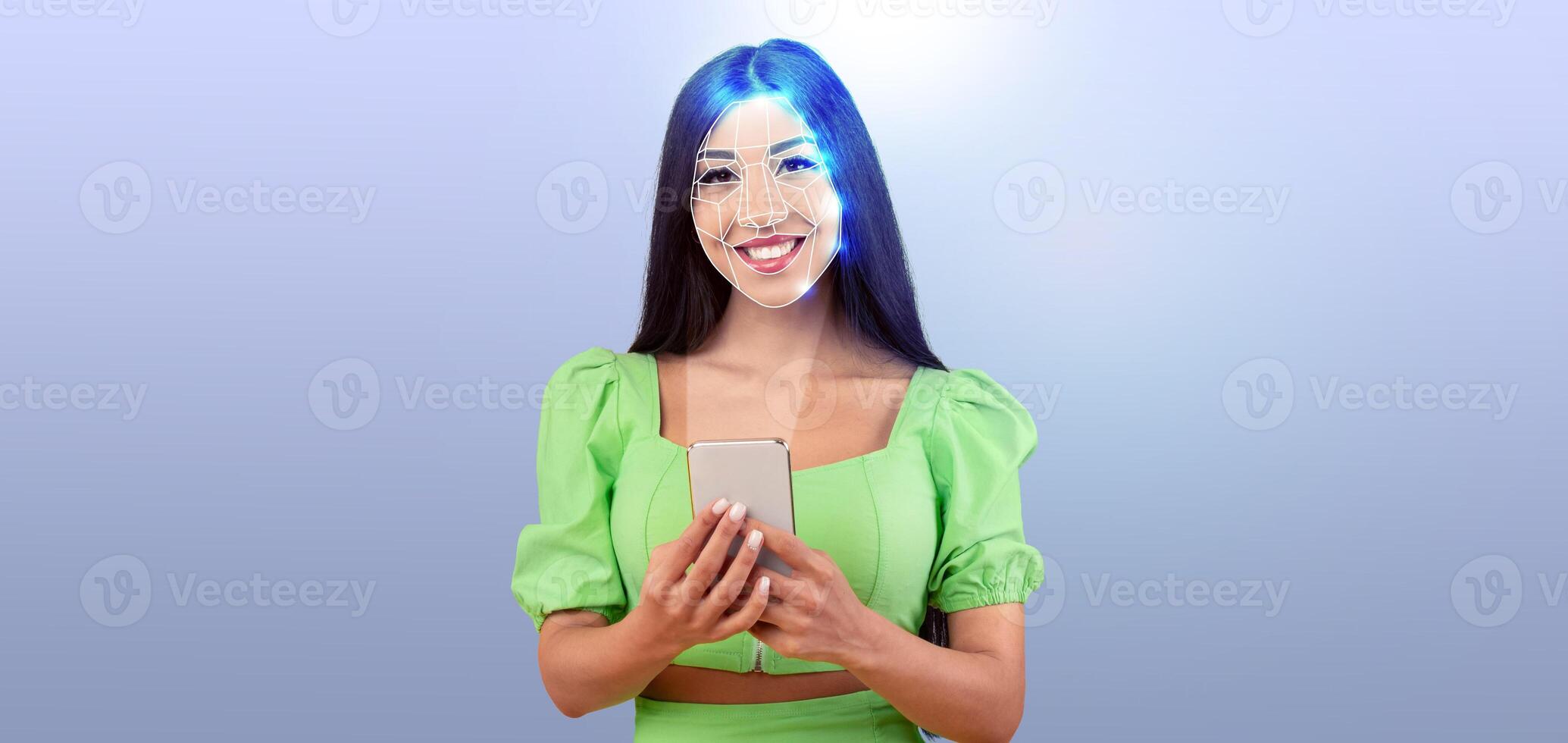 A young woman smiles while holding a smartphone, showcasing facial recognition technology. The background features an isolated, light color, highlighting her expression and the device. photo