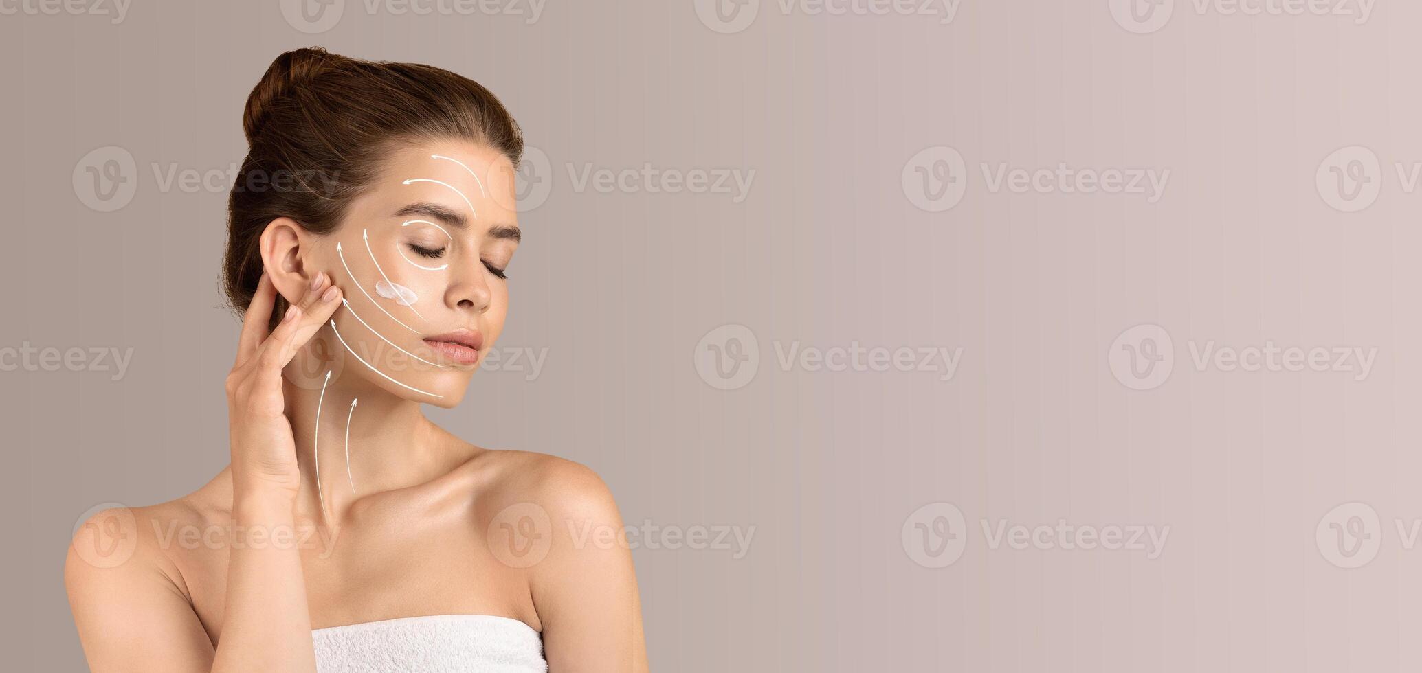 A woman engages in her beauty routine, applying skin care products to her face. She is isolated against a soft, neutral background, creating a calm and relaxing atmosphere for self-pampering. photo