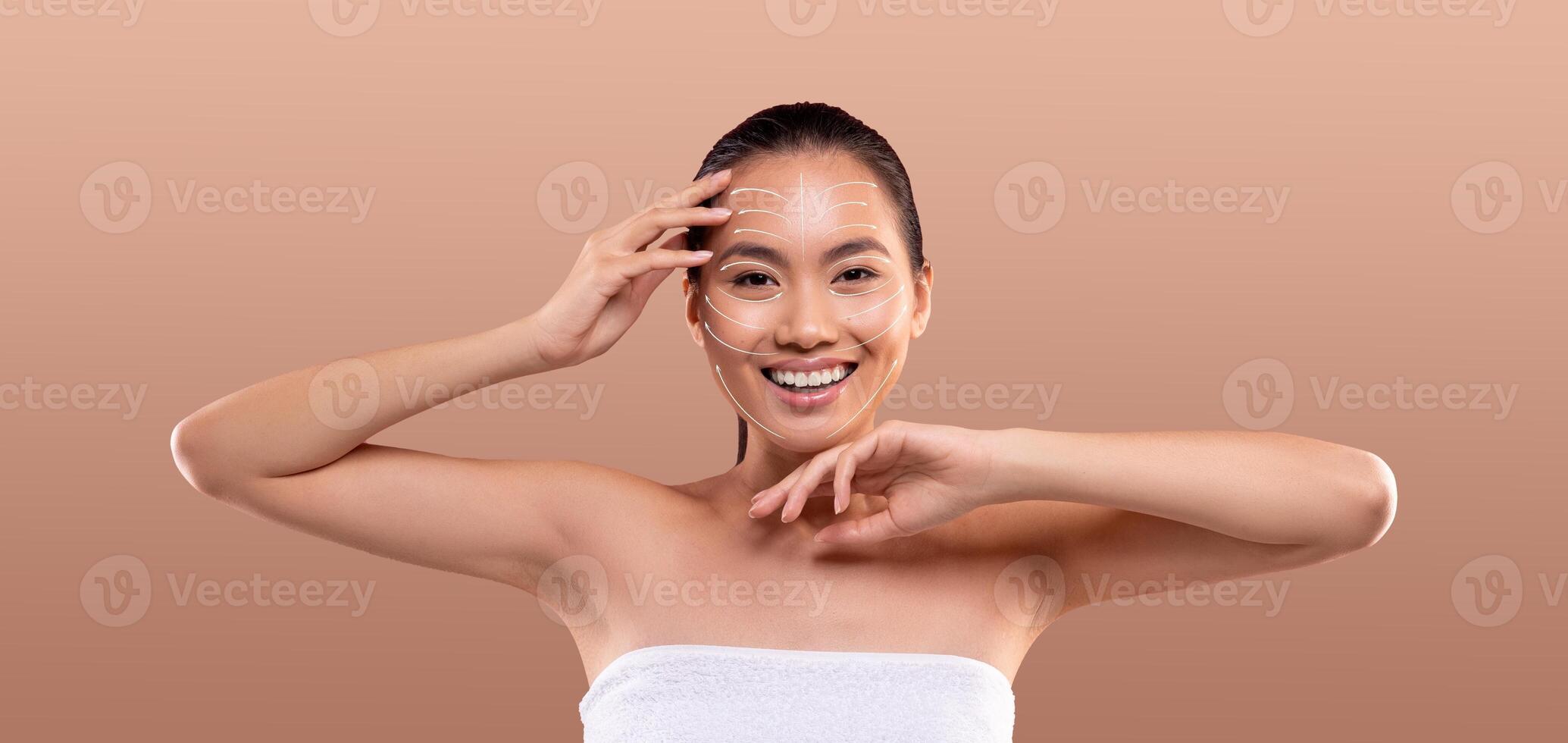 Asian woman enjoys her skincare routine, applying products to her face with a smile. She showcases the importance of self-care in a relaxed, isolated setting with ample empty space. photo