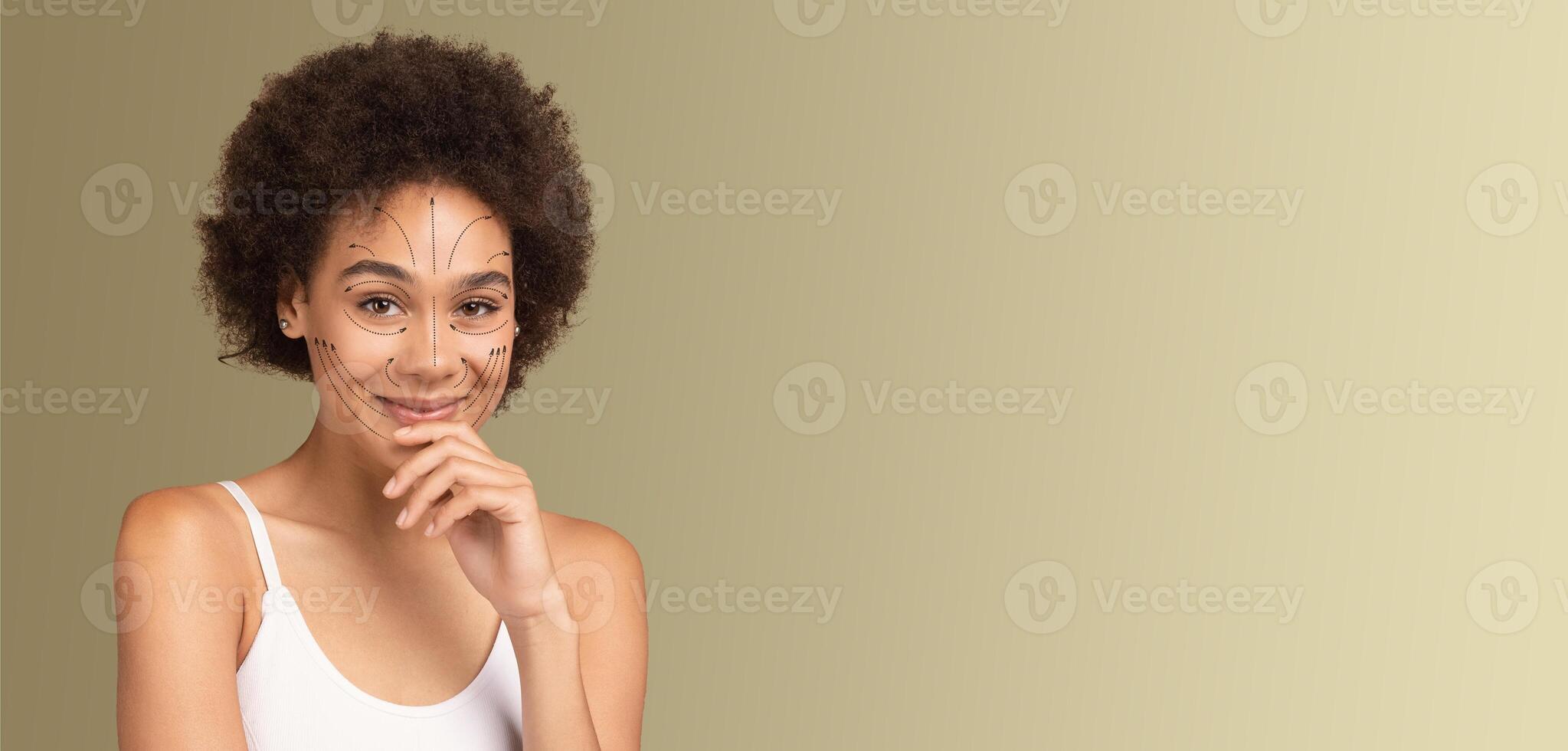 A smiling African American woman with natural beauty is engaging in a skincare routine. She is isolated against a soft, neutral backdrop, showcasing her pampering process with an air of tranquility. photo