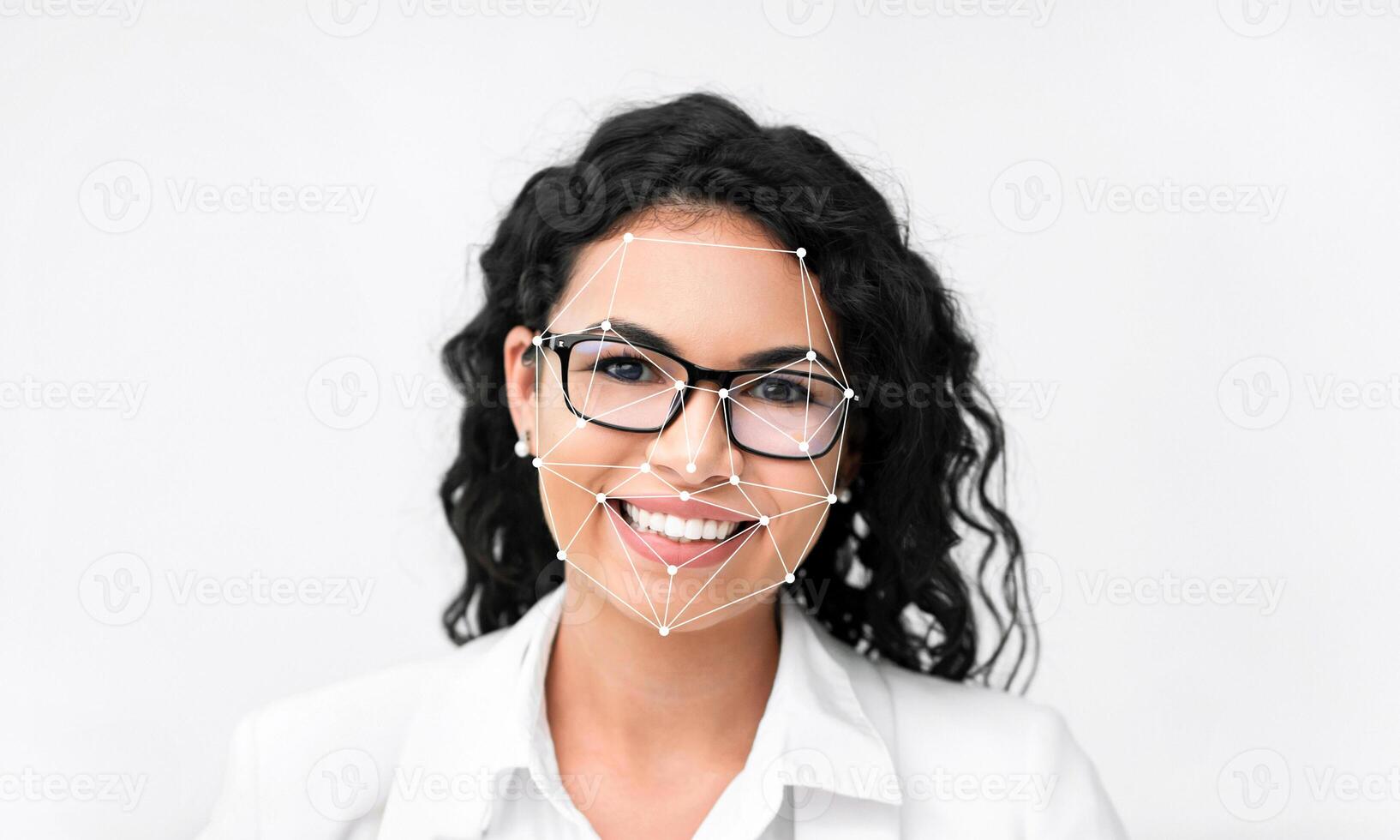 A woman with curly hair and glasses smiles while facial recognition technology analyzes her features. The background is plain, emphasizing the innovative technology highlighting her face. photo