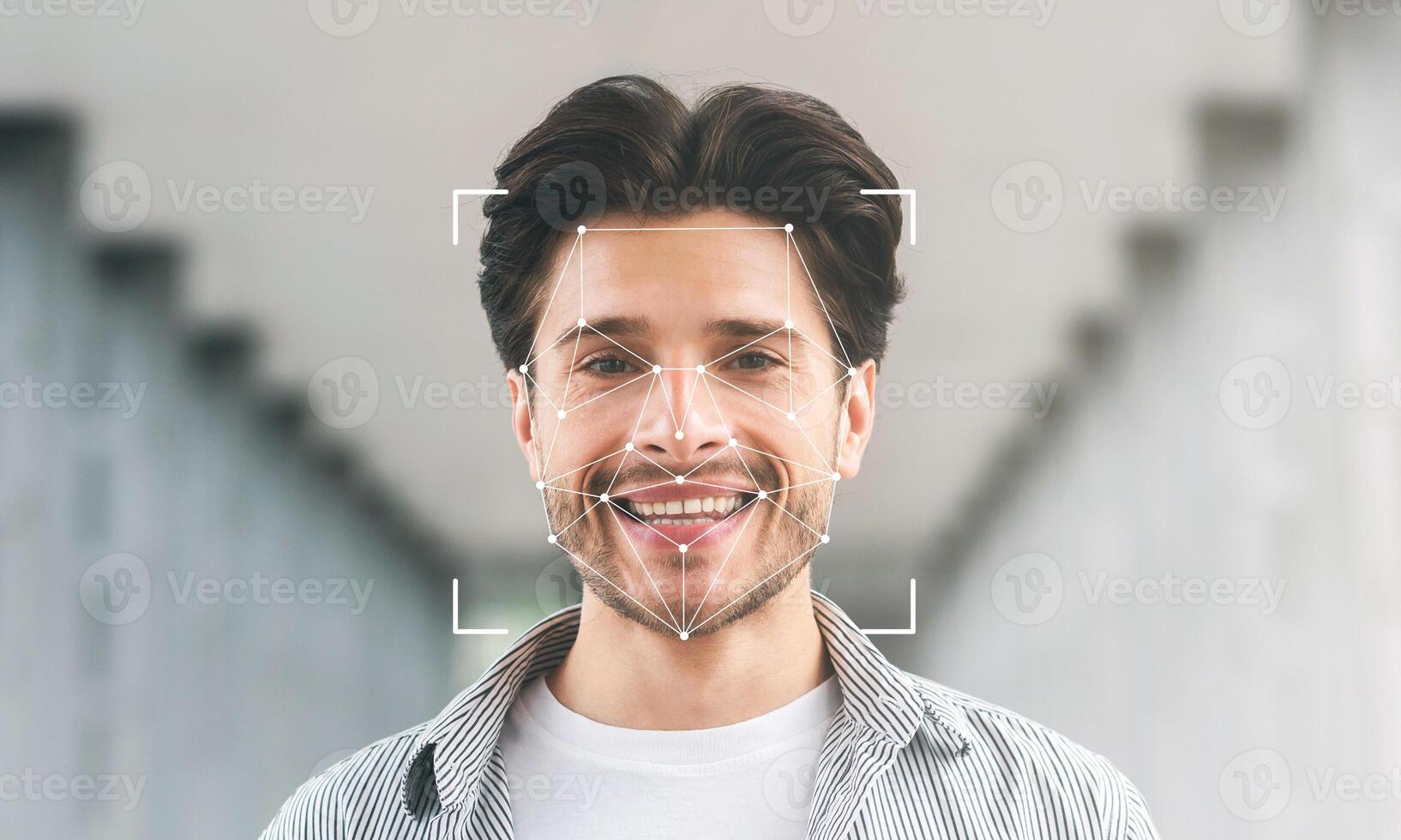 A smiling young man stands in a modern corridor, surrounded by soft lighting. His face is framed by digital facial recognition technology, highlighting identification features. photo