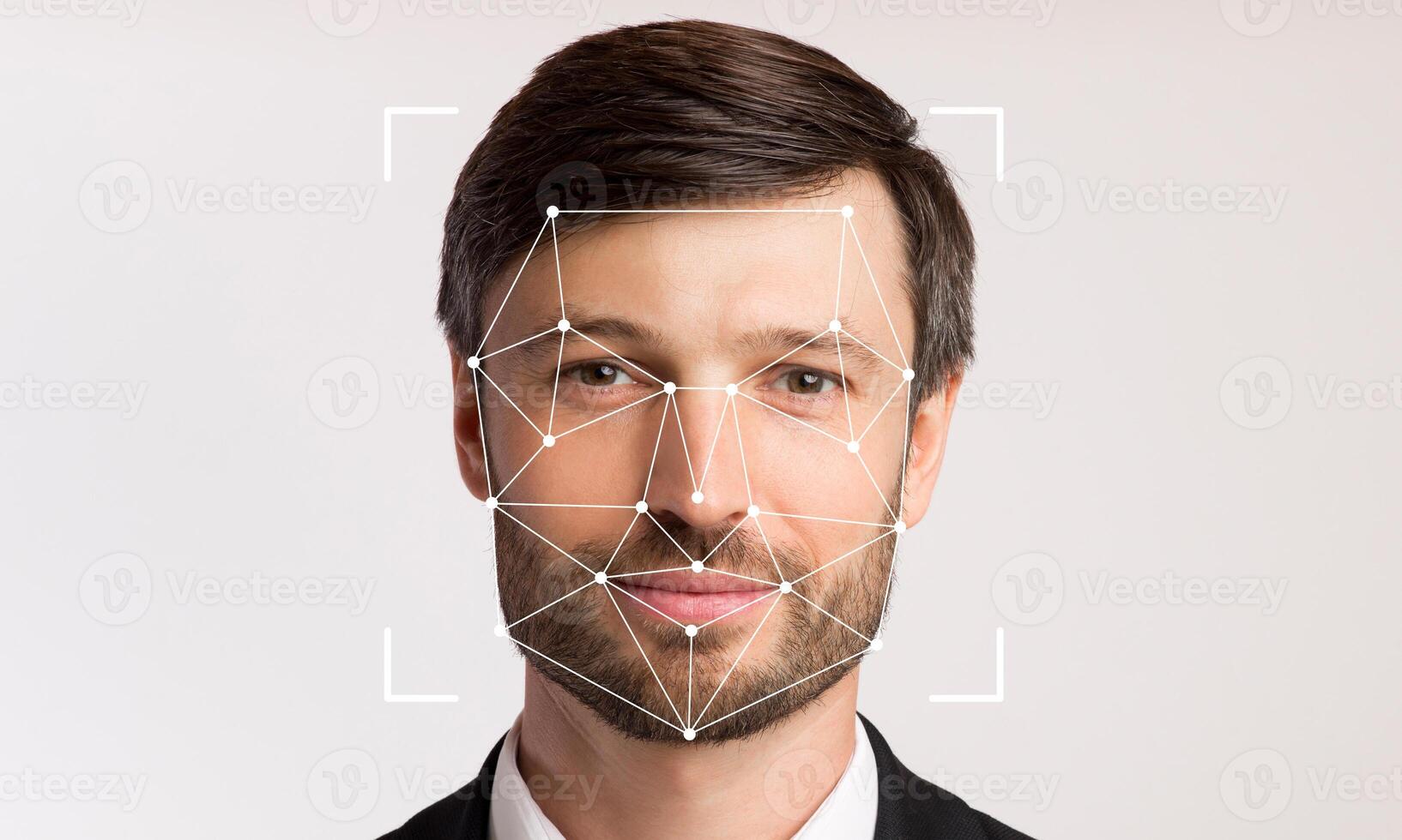 A man with a neutral expression stands against a plain background, displaying facial recognition technology that detects his facial features for identification purposes. photo