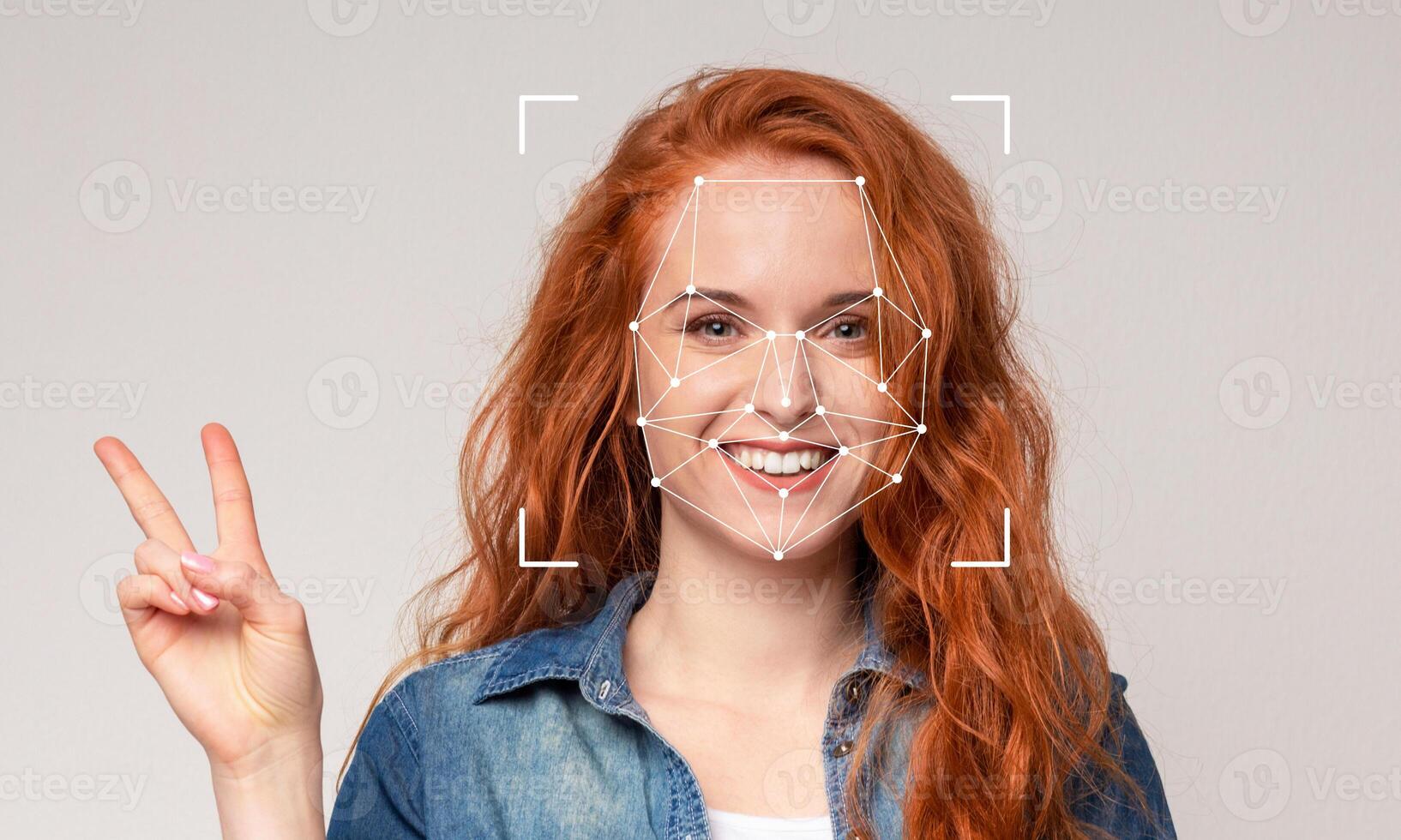 A young woman with vibrant red hair smiles widely while making a peace sign with her hand. Facial recognition markers are displayed on her face, highlighting the technology in action. photo