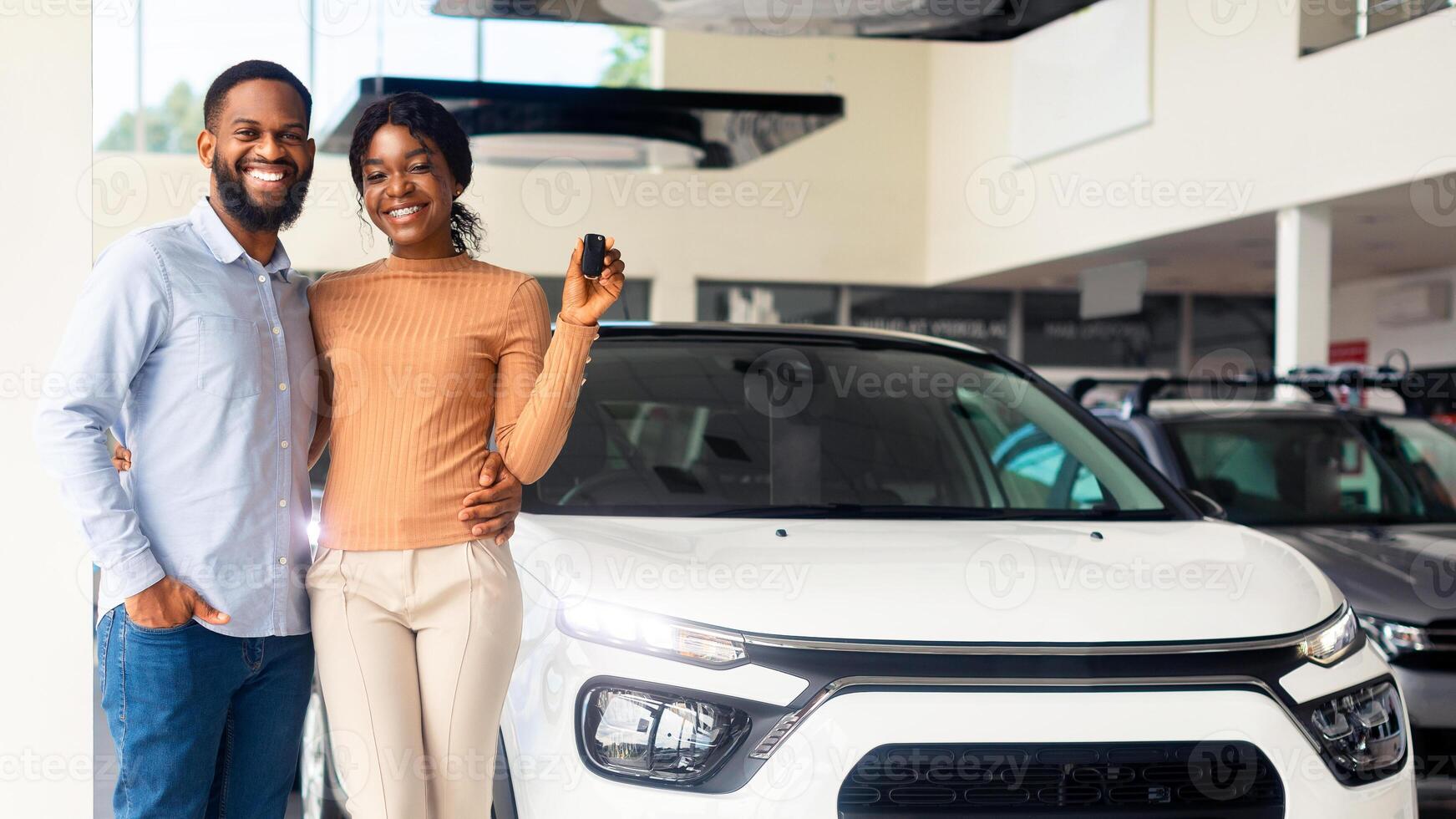 Happy African American Spouses Posing Near Luxury Car In Showroom, Cheerful Black Couple Holding Keys And Smiling At Camera, Buying New Vehicle In Modern Auto Salon, Full Length Shot, Copy Space photo