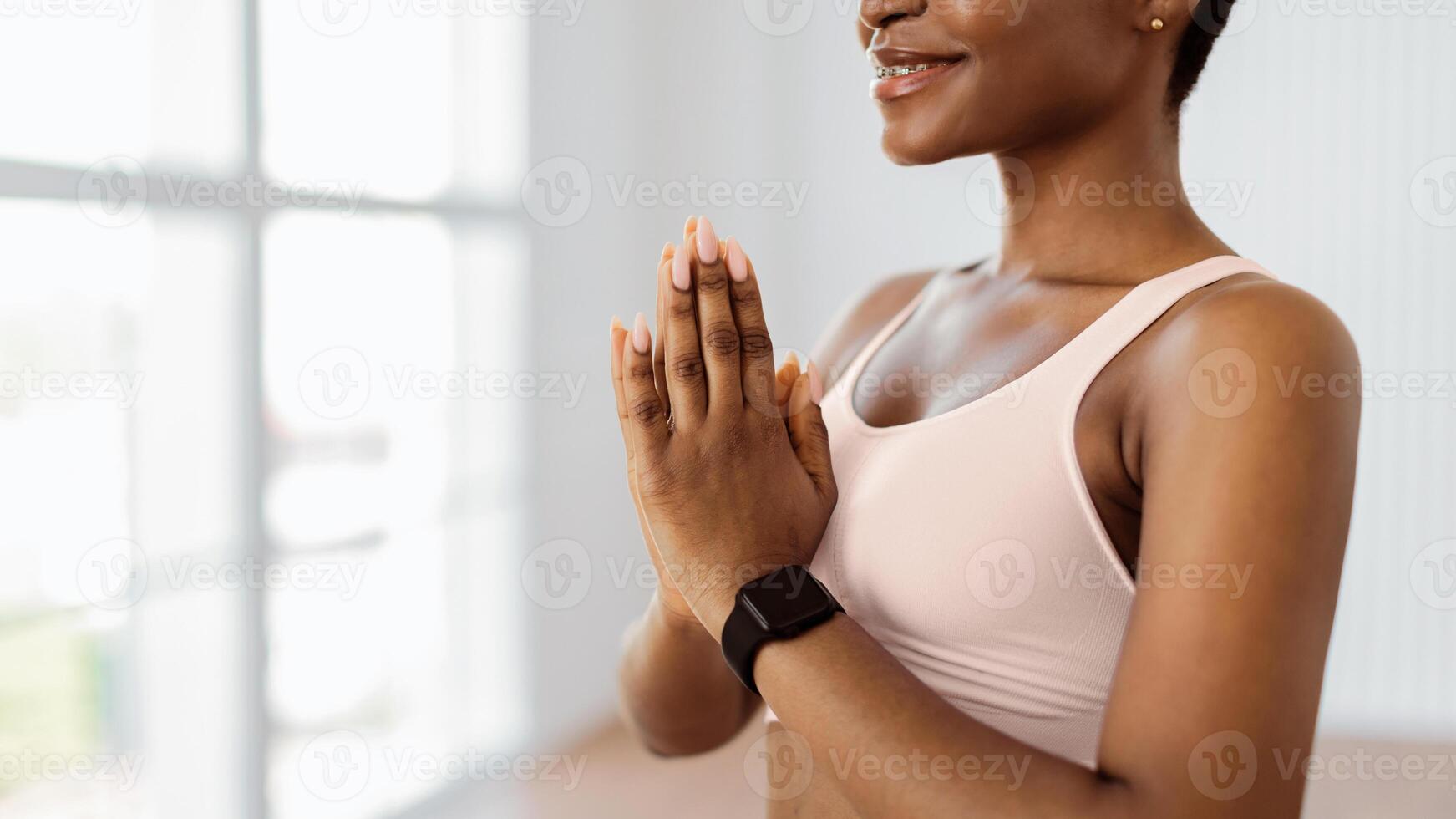 Namaste. Closeup of smiling African American woman in braces praying and meditating, sporty lady in smartwatch chanting mantra holding hands palms together, banner, panorama, free copy space photo