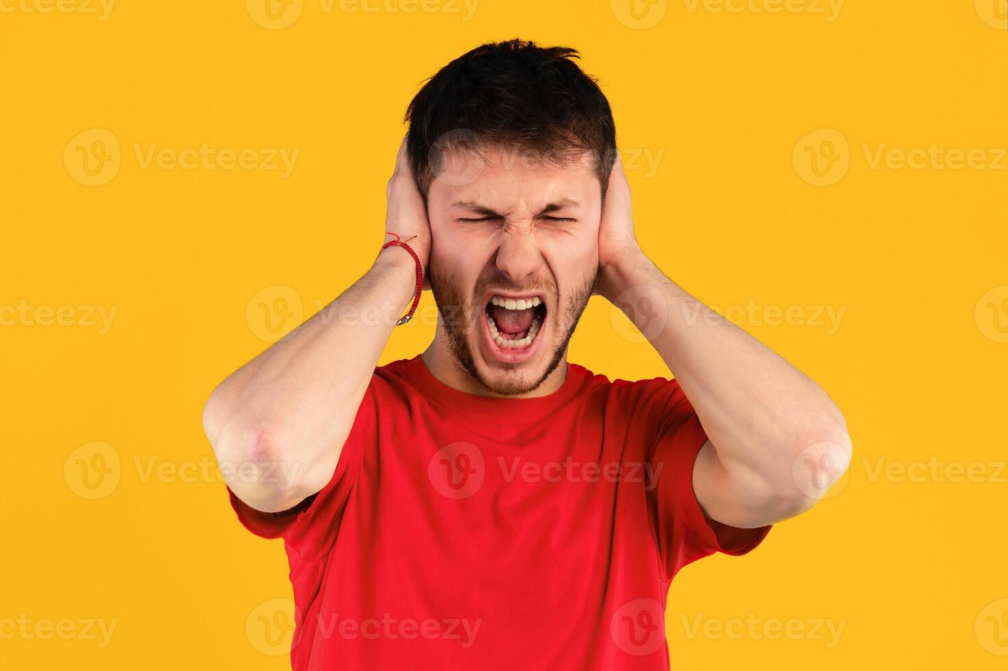 Emotions, Stress, Madness and People Concept. Crazy angry shouting man grabbing his head, screaming with closed eyes and wide open mouth, covering ears with hands over blue studio background photo
