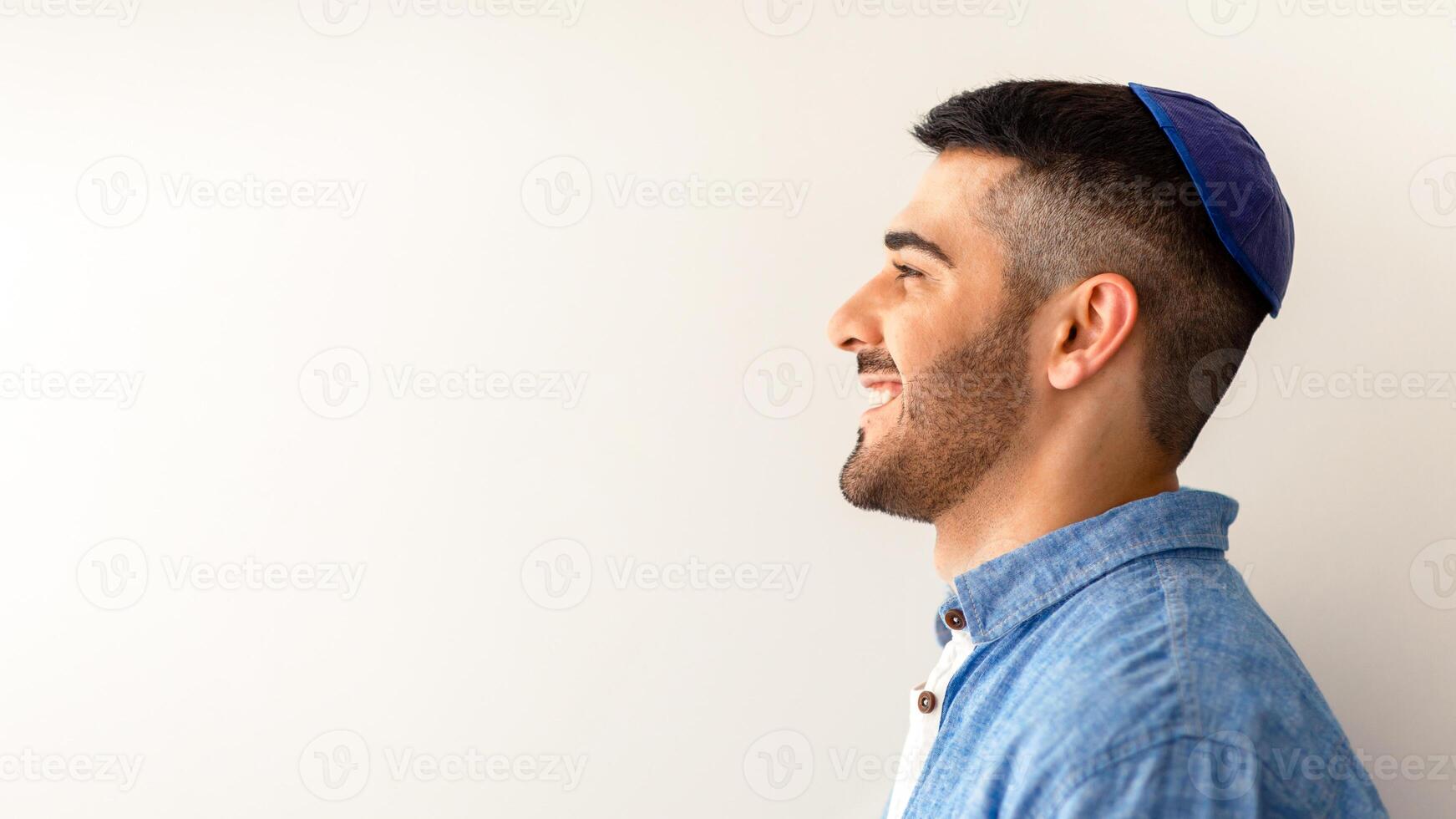 Happy Person. Profile side view portrait of handsome cheerful jewish guy posing at studio, smiling and looking aside, wearing kipa, posing isolated on light background copy free space, advert banner photo