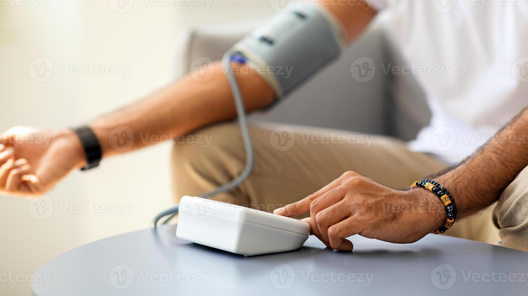 Closeup of unrecognizable man in white t-shirt using modern tonometer at home, copy space. Cropped of middle-eastern male patient measuring his blood pressure, making self checkup photo