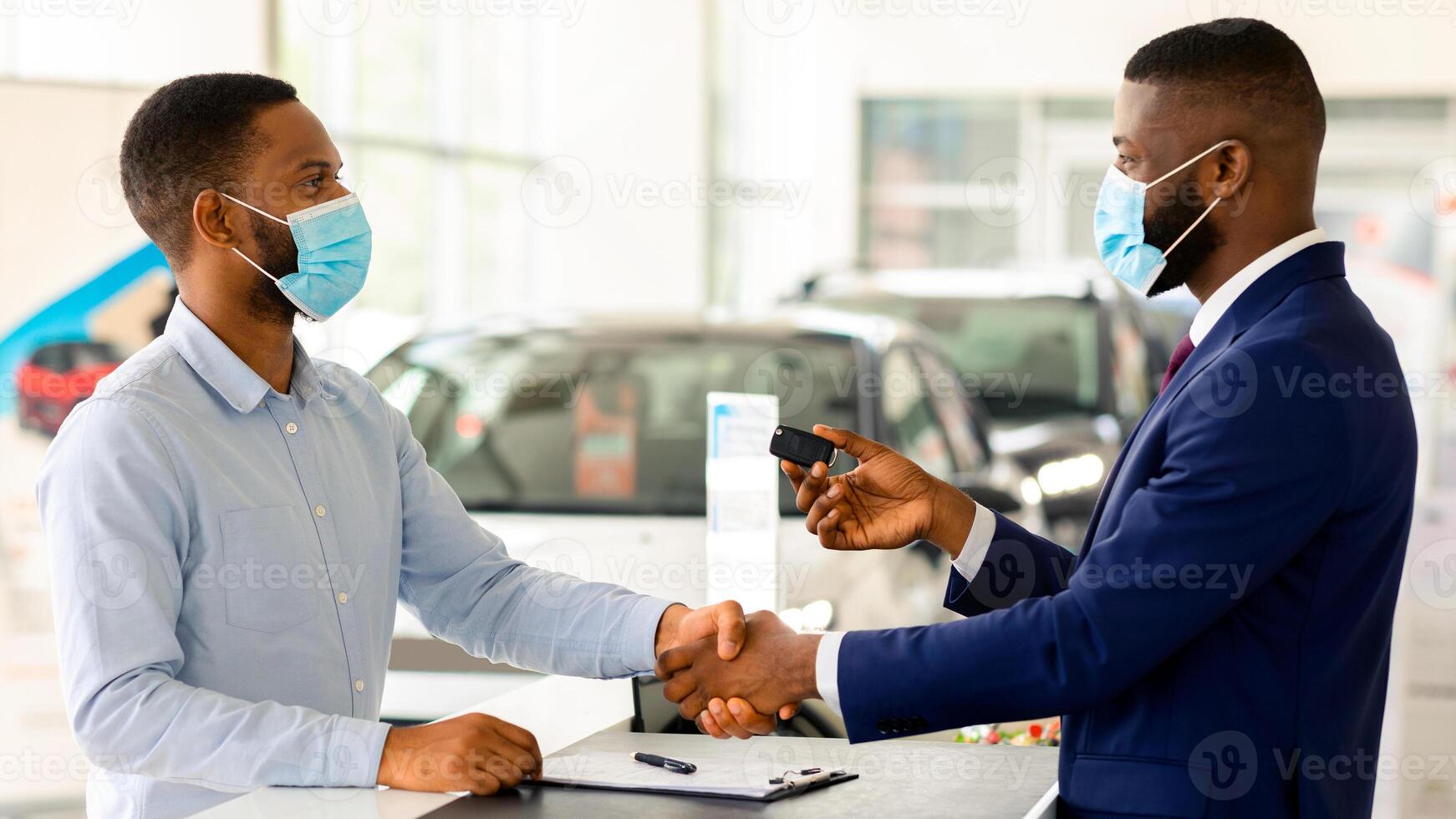 Car Sales. Black Salesman In Medical Mask Giving Key To Customer In Dealership Center, African American Man Buying New Vehicle During Coronavirus Pandemic, Handshaking With Salesperson After Deal photo