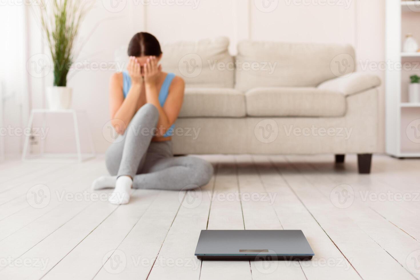Woman Crying Sitting Near Weight Scales Gaining Kilograms At Home. Selective Focus, Shallow Depth, Free Space photo