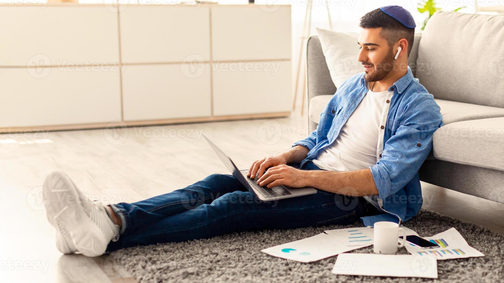 Workplace. Young Jewish Employee Working On Laptop Sitting On Floor Carpet, Busy Male Entrepreneur Typing On Keyboard And Looking At Computer Screen, Checking Email Doing Online Project, Free Space photo