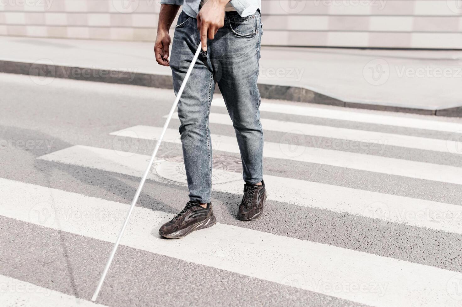 Unrecognizable young black man with vision disability walking across city street, using walking cane outdoors, copy space. Millennial blind guy crossing road alone, cropped view photo