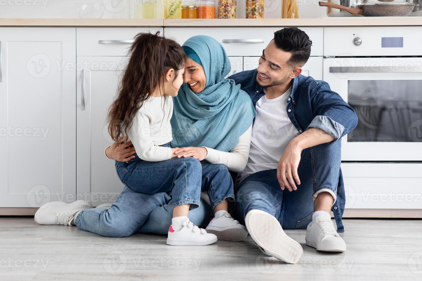 Happy Islamic Parents Bonding With Their Little Daughter In Kitchen, Portrait Of Cheerful Smiling Middle Easter Family Of Three Relaxing On Floor, Enjoying Spending Time Together, Free Space photo
