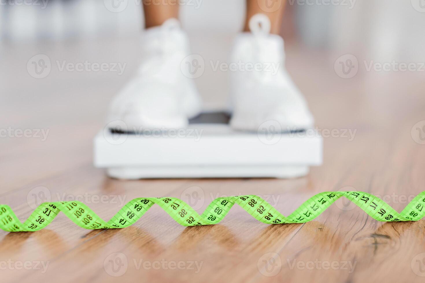 Weight Control Concept. Selective focus on yellow measuring tape on the floor and blurred view of african woman standing on scales, checking result of her slimming diet. Dieting, healthy living photo