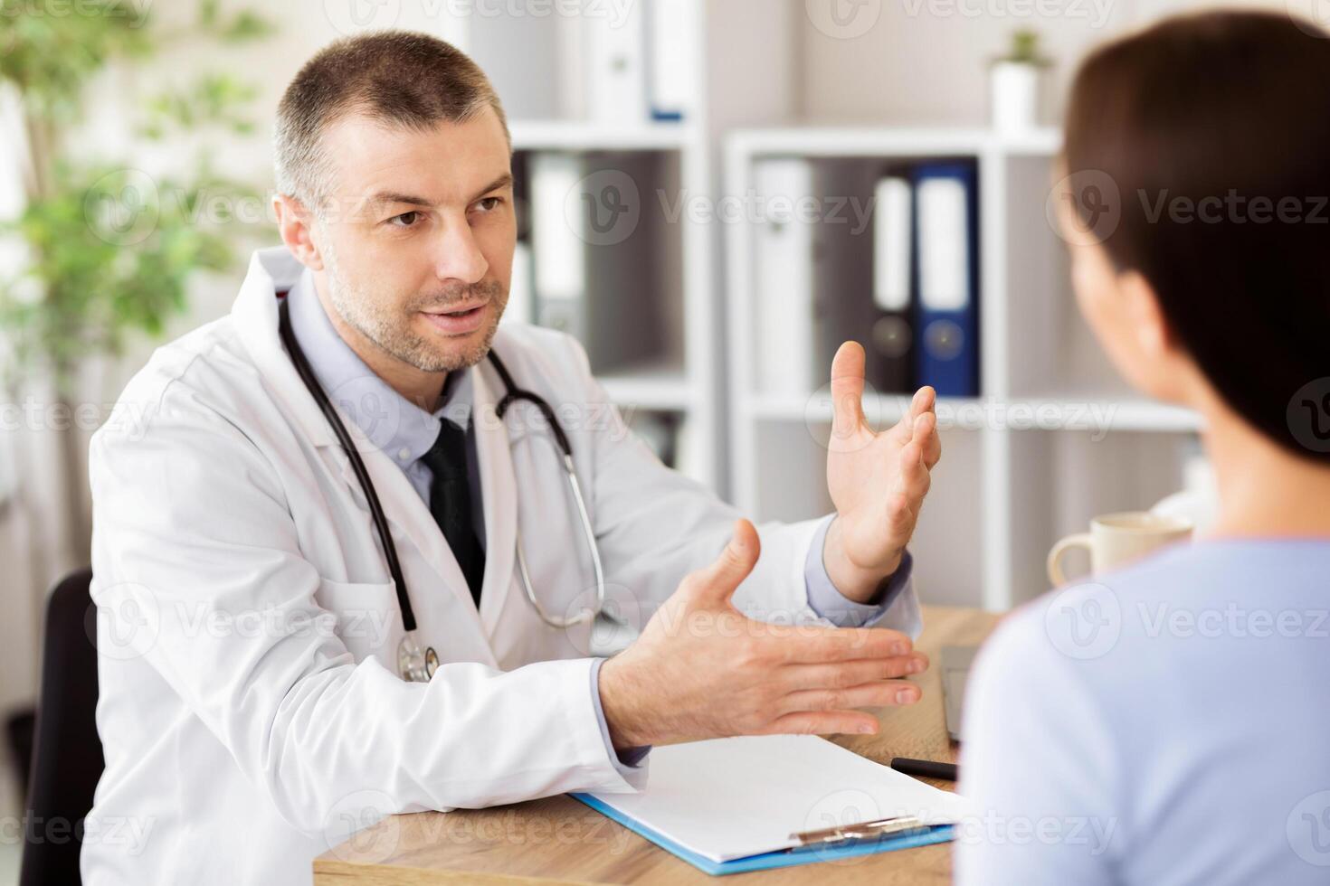 General Practitioner Appointment. Portrait of male doctor talking to his patient, discussing diagnosis and treatment. Specialist giving consultation to woman, sitting at desk in his office photo