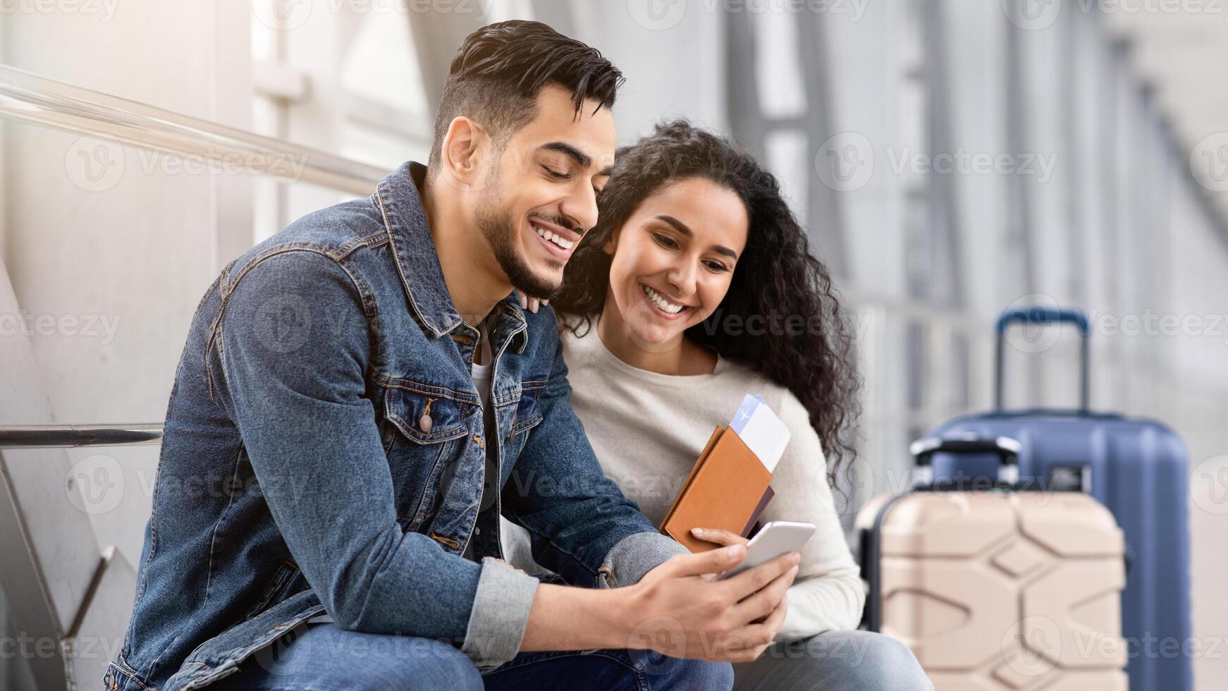Waiting For Flight. Young Arab Spouses Using Smartphone In Airport Terminal, Middle Eastern Couple Browsing Internet On Mobile Phone Or Booking Hotel Online Before Flight Boarding, Closeup Shot photo