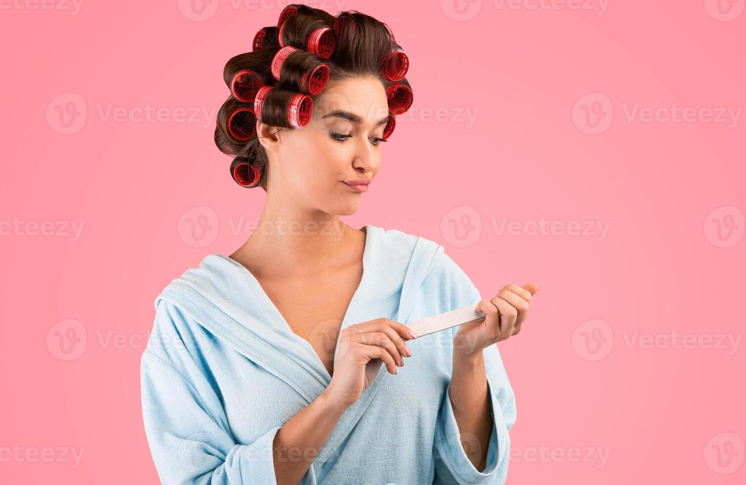 Displeased Housewife Doing Manicure With Nail Buffer Standing On Yellow Background. Studio Shot photo
