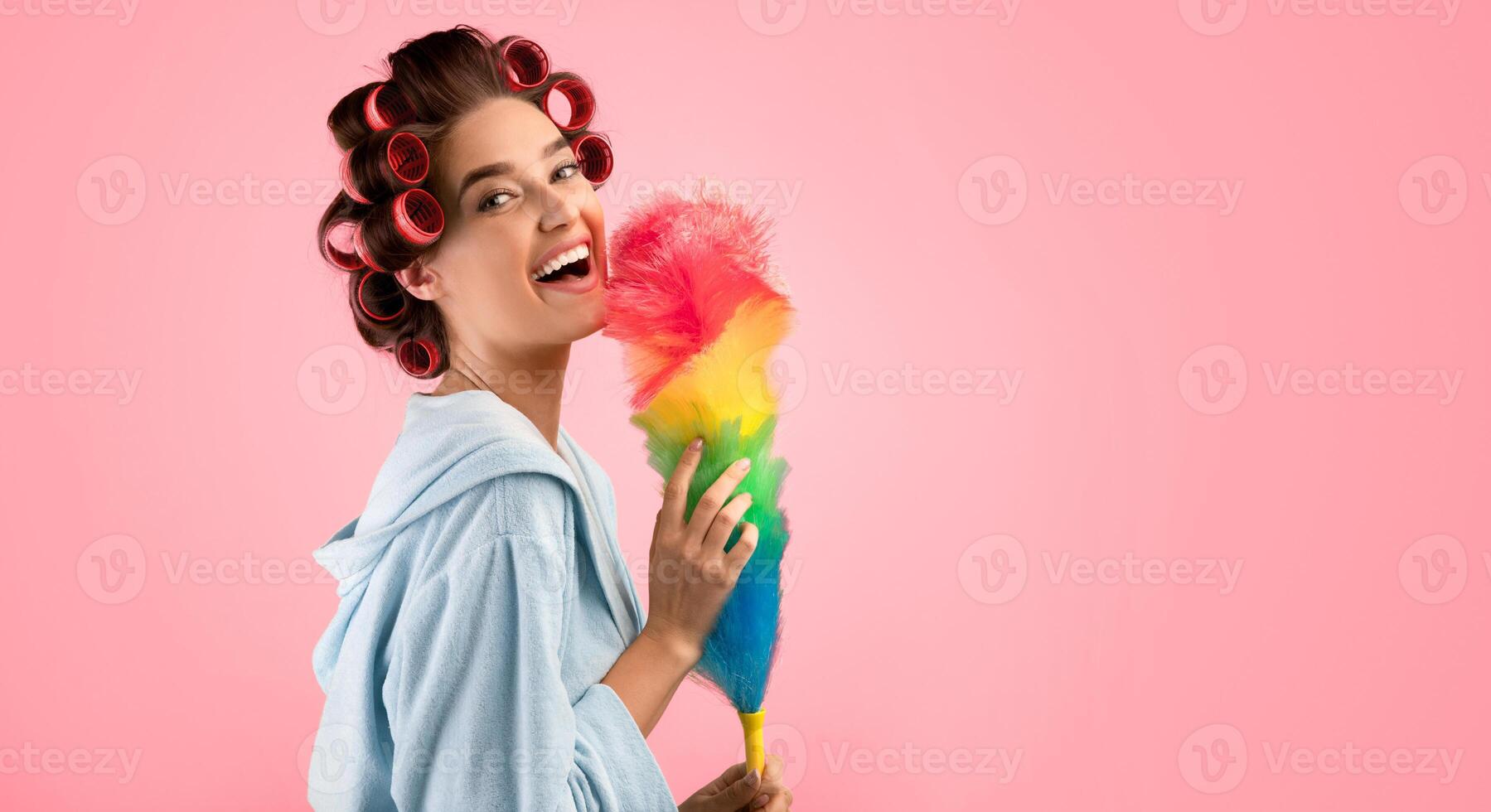 Spring Cleaning. Happy Glamorous Woman With Hair Curlers Holding Feather Duster Smiling To Camera Doing Housework Standing Over Yellow Studio Background. House Chores Concept. Panorama, Free Space photo