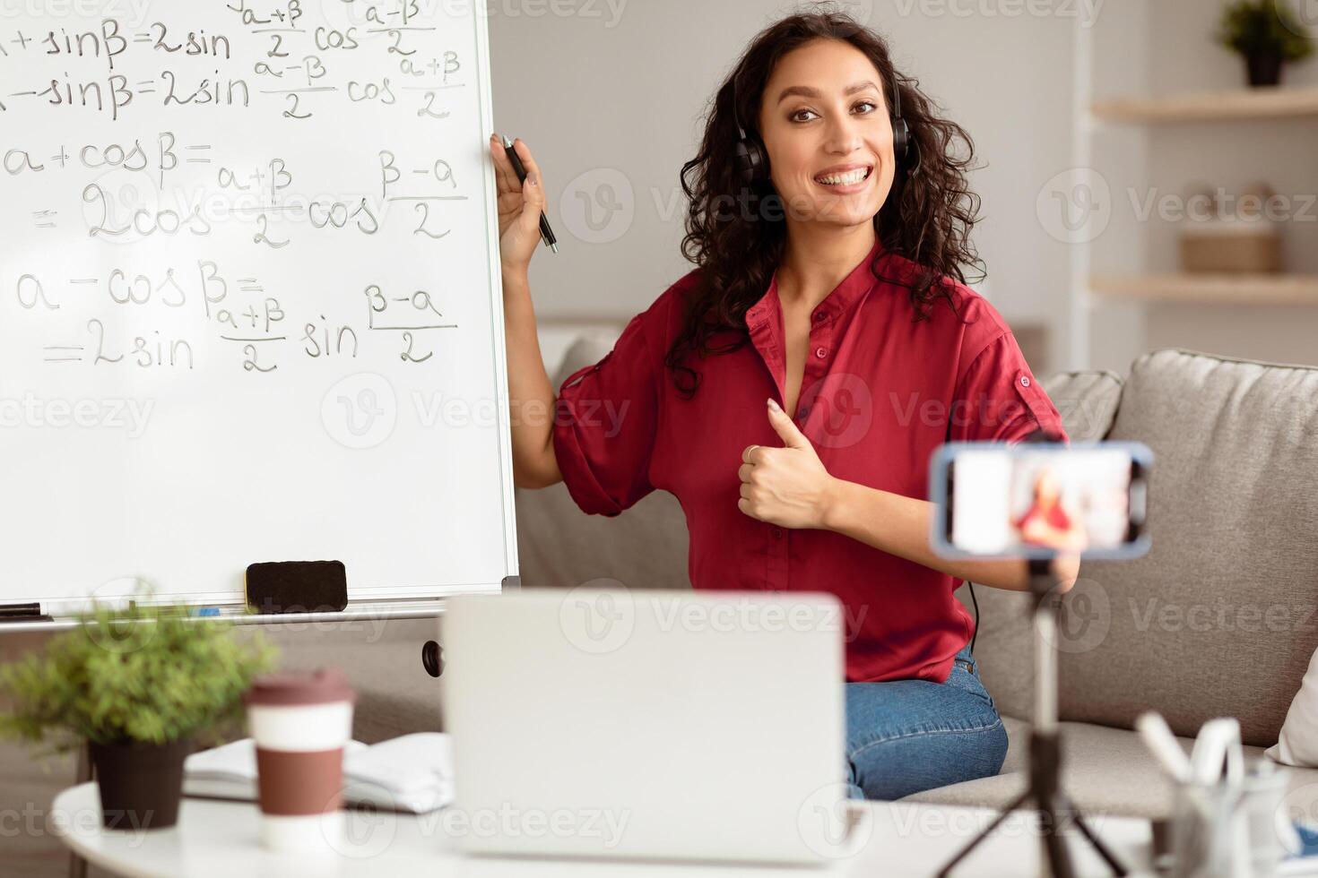 Lady teacher recommending online school, showing thumb up gesture sign, giving virtual lesson, explaining math. Positive young tutor satisfied with educational services, recording on cellphone photo