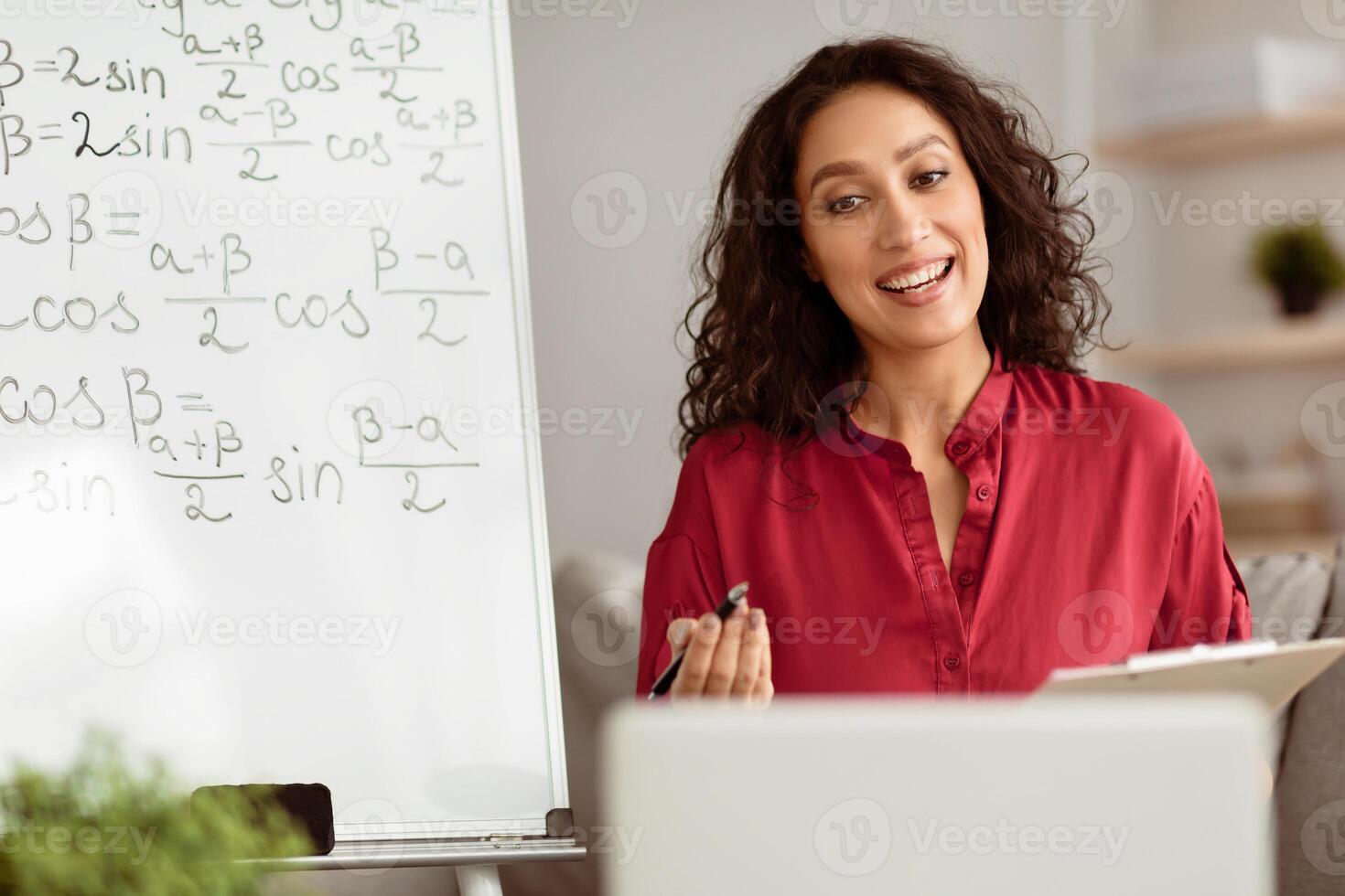 Portrait of smiling millennial teacher giving online lesson on laptop from home, talking looking at webcam, blogger recording vlog. Young math tutor participating in educational web conference on pc photo