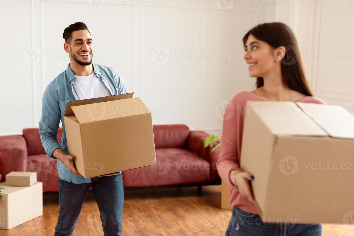 Loving couple carrying cardboard boxes together, helping each other in their new home on moving day. Young tenants relocating to new apartment with belongings, unpacking things in living room photo