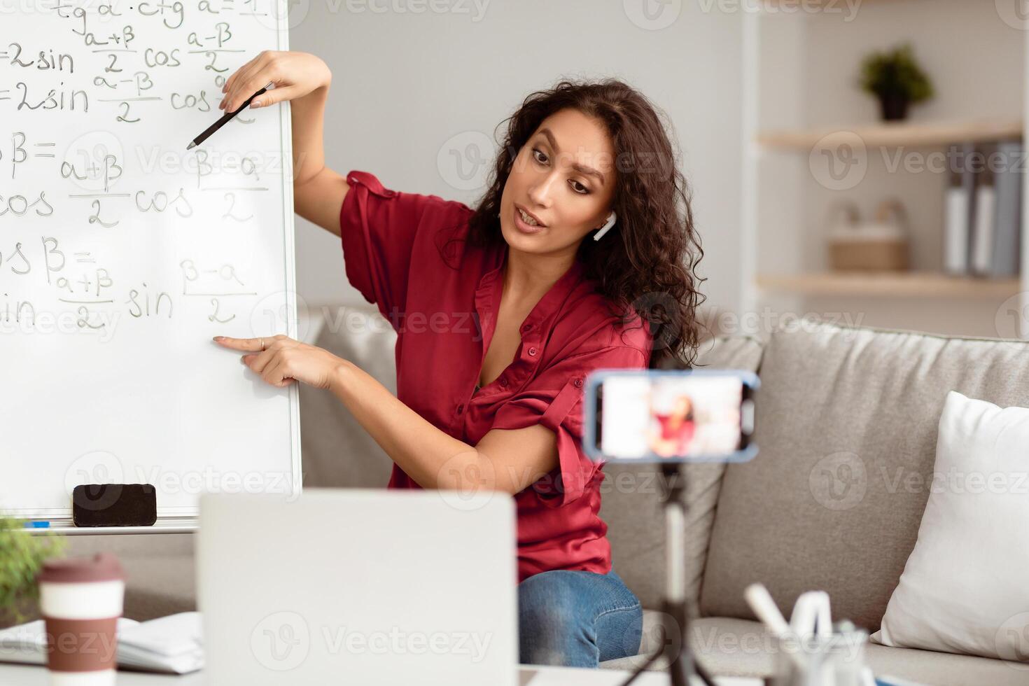Modern Teacher. Woman In Earphones Filming Virtual Lecture For Educational Blog Sitting In Front Of Laptop And Mobile Camera Indoors. Remote Tutoring And E-Teaching Concept. Live Streaming photo