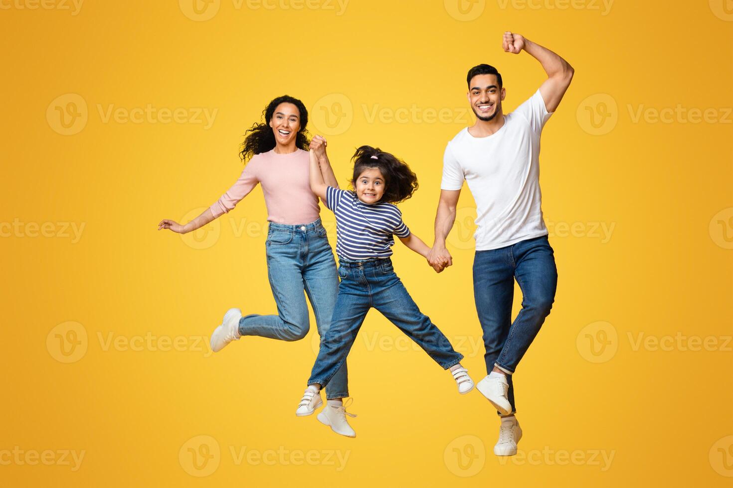 Crazy Offer. Portrait Of Funny Young Arab Family With Little Daughter Jumping Over Yellow Background, Cheerful Middle Eastern Parents And Cute Female Child Having Fun Together In Studio, Copy Space photo
