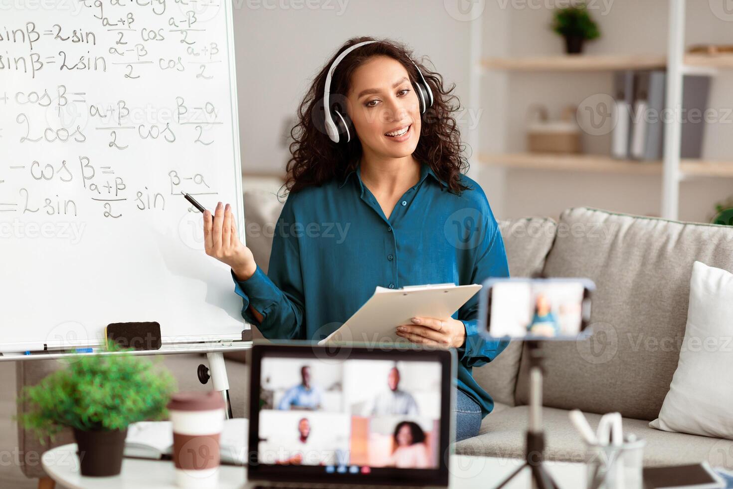 Online Training. Young lady tutor in headset teaching online by conference using laptop and smartphone. Teacher explaining information to diverse participants in the virtual conference photo