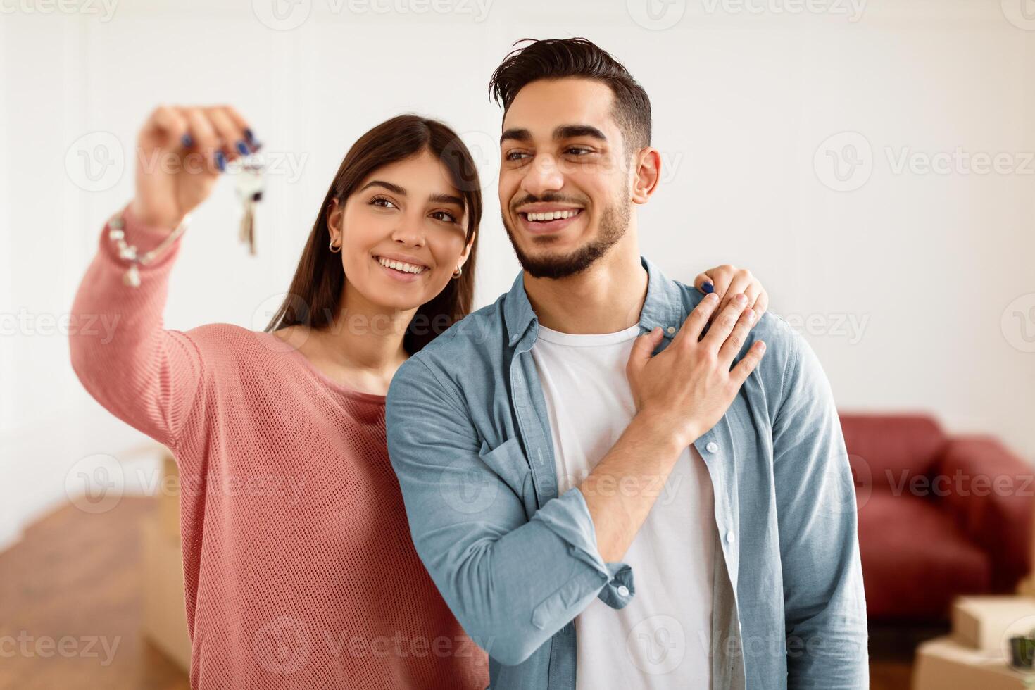House Ownership. Portrait Of Excited Young Couple Holding And Showing Keys, Cheerful Guy And Lady Hugging After Moving In New Apartment Standing In Living Room. Insurance, Real Estate Mortgage Concept photo