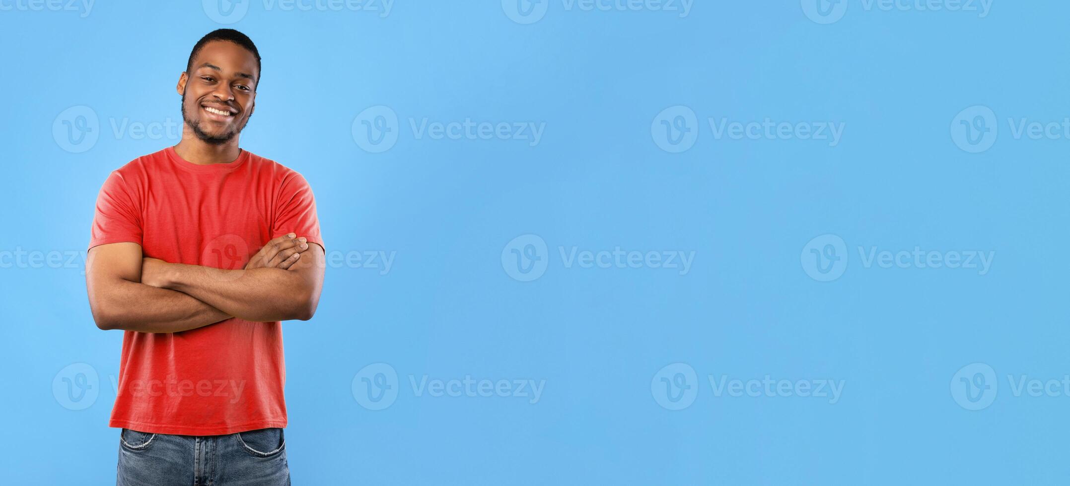 Cheerful African American Guy Smiling To Camera Posing Crossing Hands Standing Over Blue Background. Studio Shot Of Happy Self-Confident Black Millennial Man Expressing Positive Emotions photo