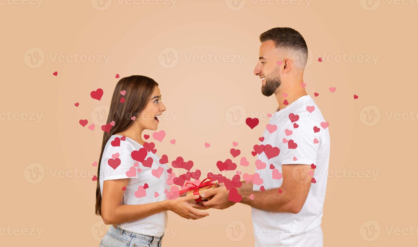 A couple joyfully exchanges a gift, displaying affection and excitement. Surrounding them are floating hearts, symbolizing their bond and celebration of love on Valentine's Day. photo
