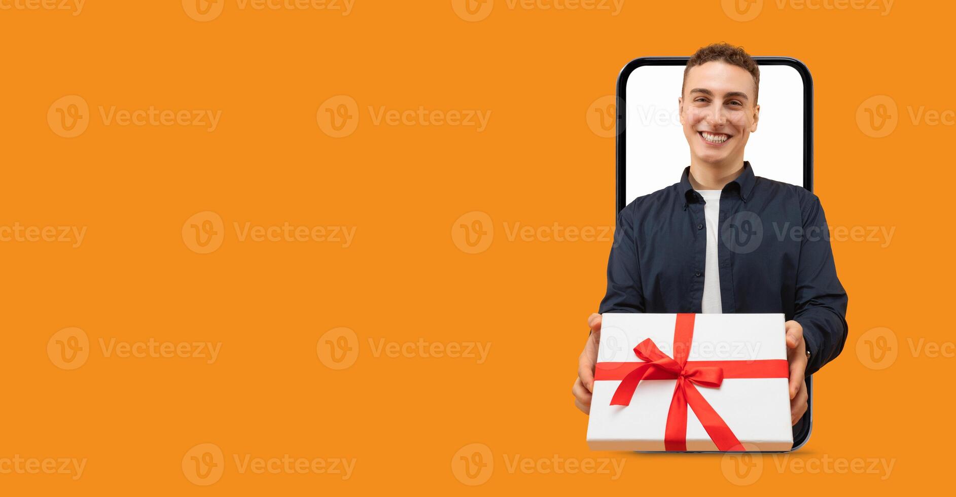 A smiling individual is holding a wrapped gift box with a red bow, appearing to come out of a smartphone screen. The background features a vibrant, solid color, emphasizing the joyful moment. photo
