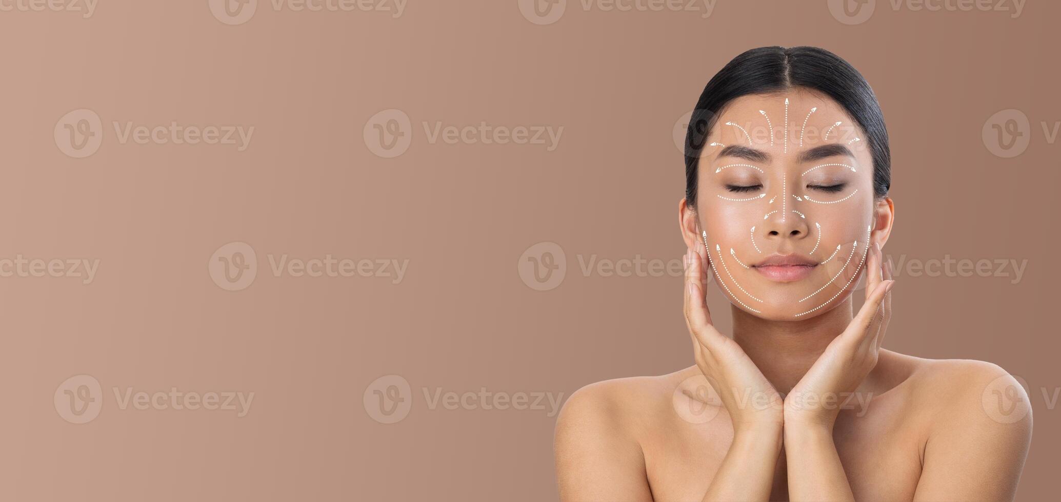 Asian woman is enjoying her skin care routine, applying techniques with her hands gently on her face. She is in a tranquil environment with a neutral background, emphasizing relaxation and pampering. photo