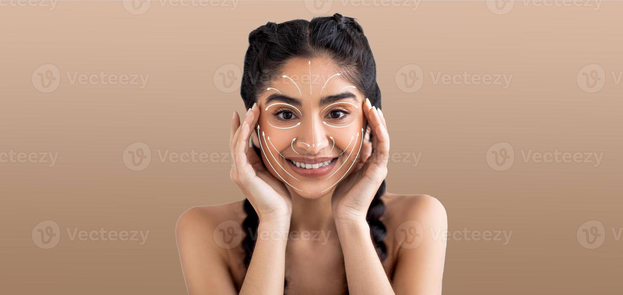 Indian woman enjoys her skin care routine, smiling and engaging in a pampering activity. She holds her face, highlighting her beauty regime in an isolated setting with soft, neutral tones. photo
