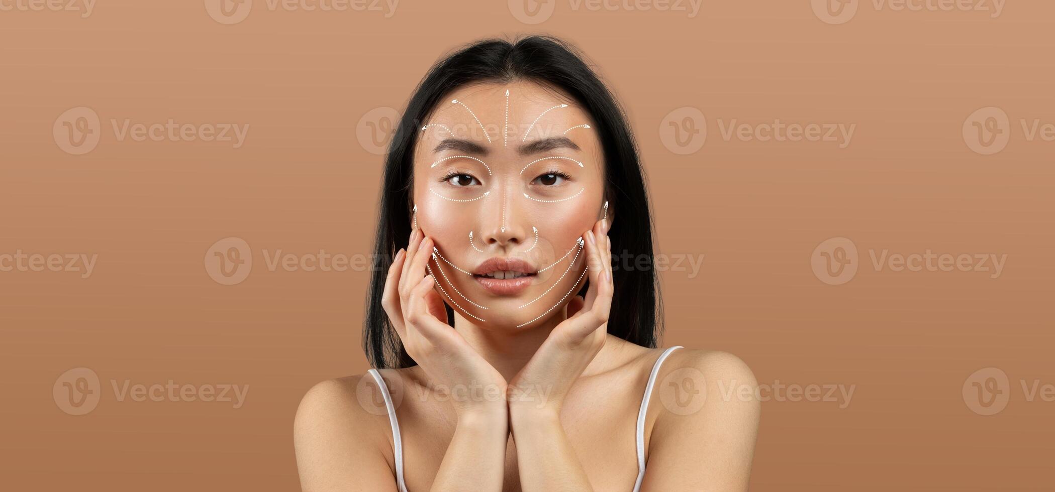 Asian woman practices her skincare routine, gently touching her face. She appears relaxed and focused, surrounded by an empty, neutral backdrop that emphasizes her beauty and self-care. photo