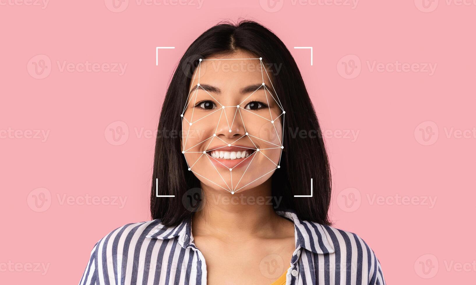 A young woman smiles as her facial features are mapped for identification purposes. The background is a solid pink color, enhancing the focus on her face and the technology used. photo