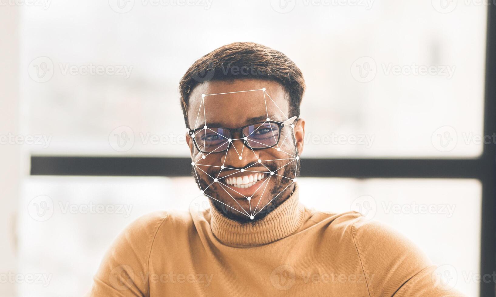 A smiling man wearing glasses sits comfortably in a well-lit indoor space. Graphic overlays illustrate facial recognition technology, highlighting features for identification. photo