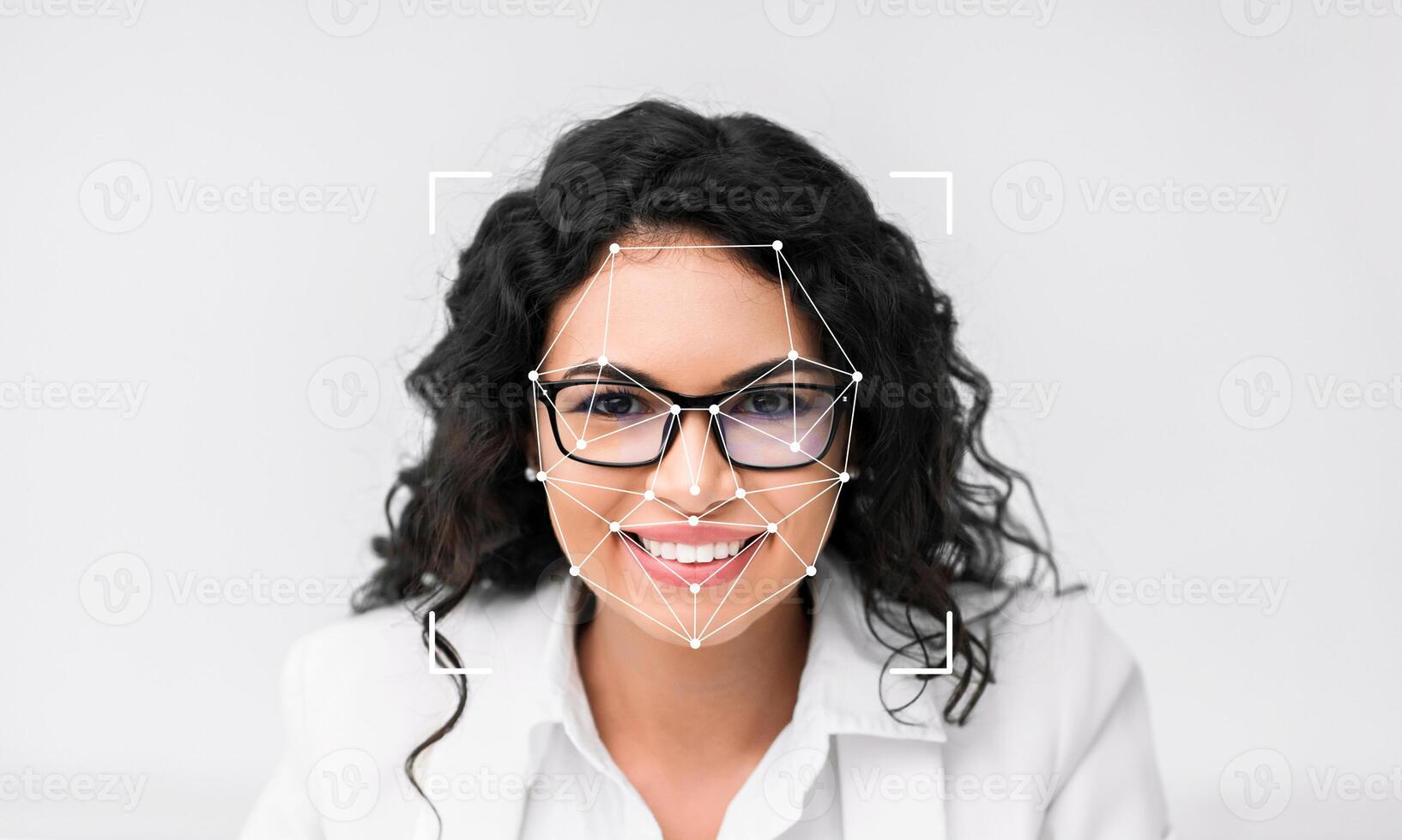 A woman smiling at the camera demonstrates facial recognition technology. Her facial features are being analyzed with an overlay marking key points for identification. The space around her is empty. photo